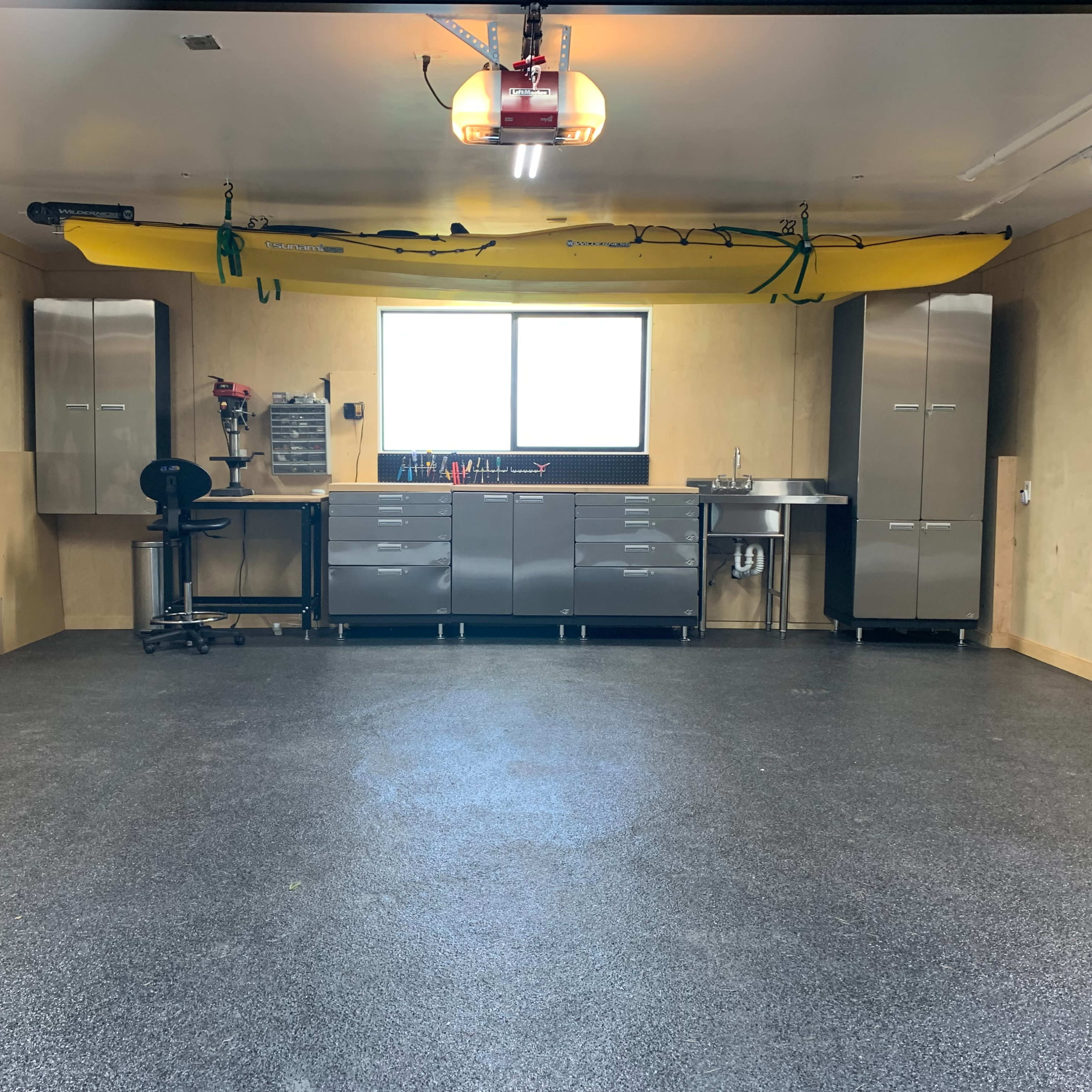 A spacious garage with gray walls, a yellow kayak suspended from the ceiling, and metal cabinets along the back wall.