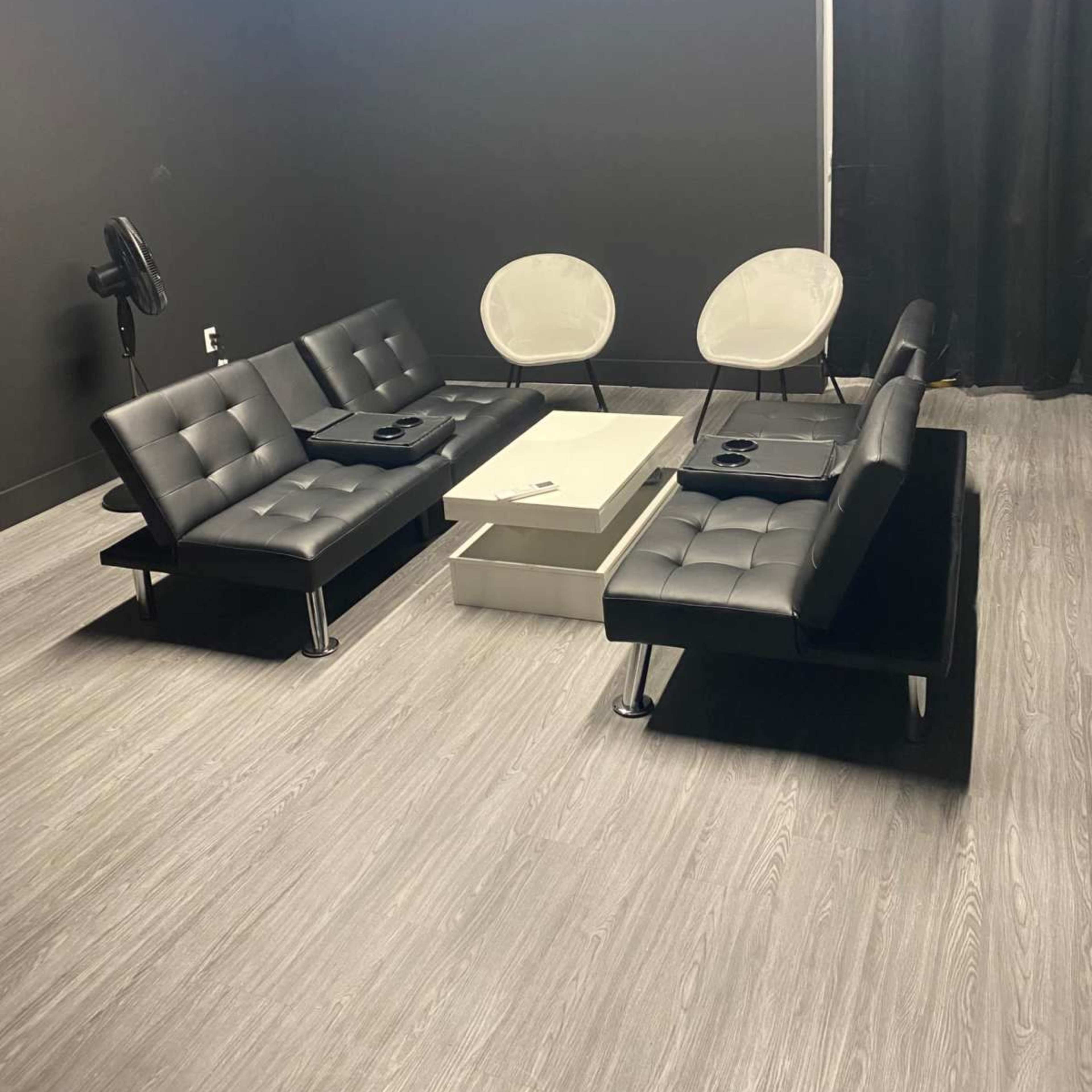 A modern lounge area with four black and gray seating options arranged around a coffee table in a dimly lit room.