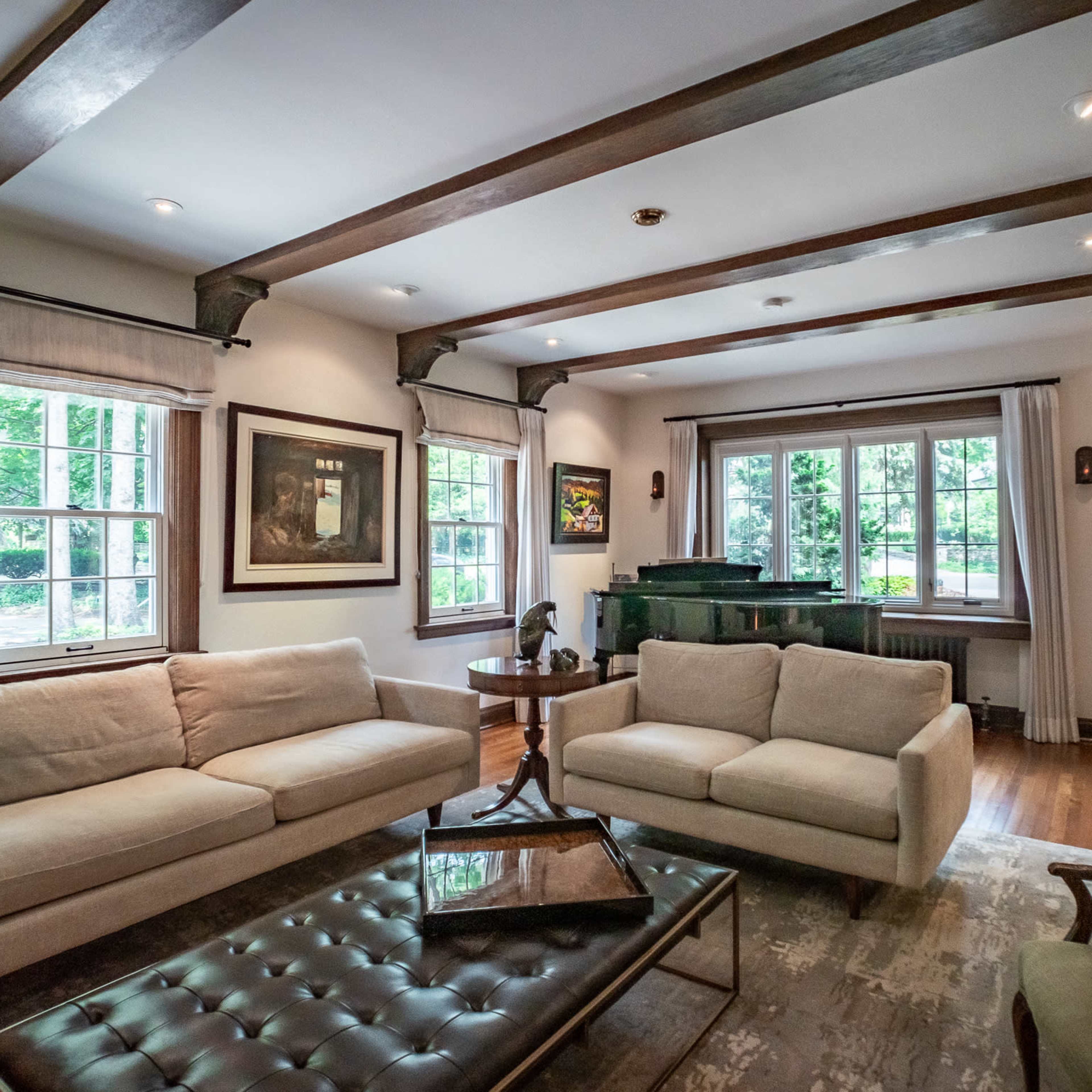 A living room with two sofas, a glass coffee table, and a piano near large windows that provide natural light.