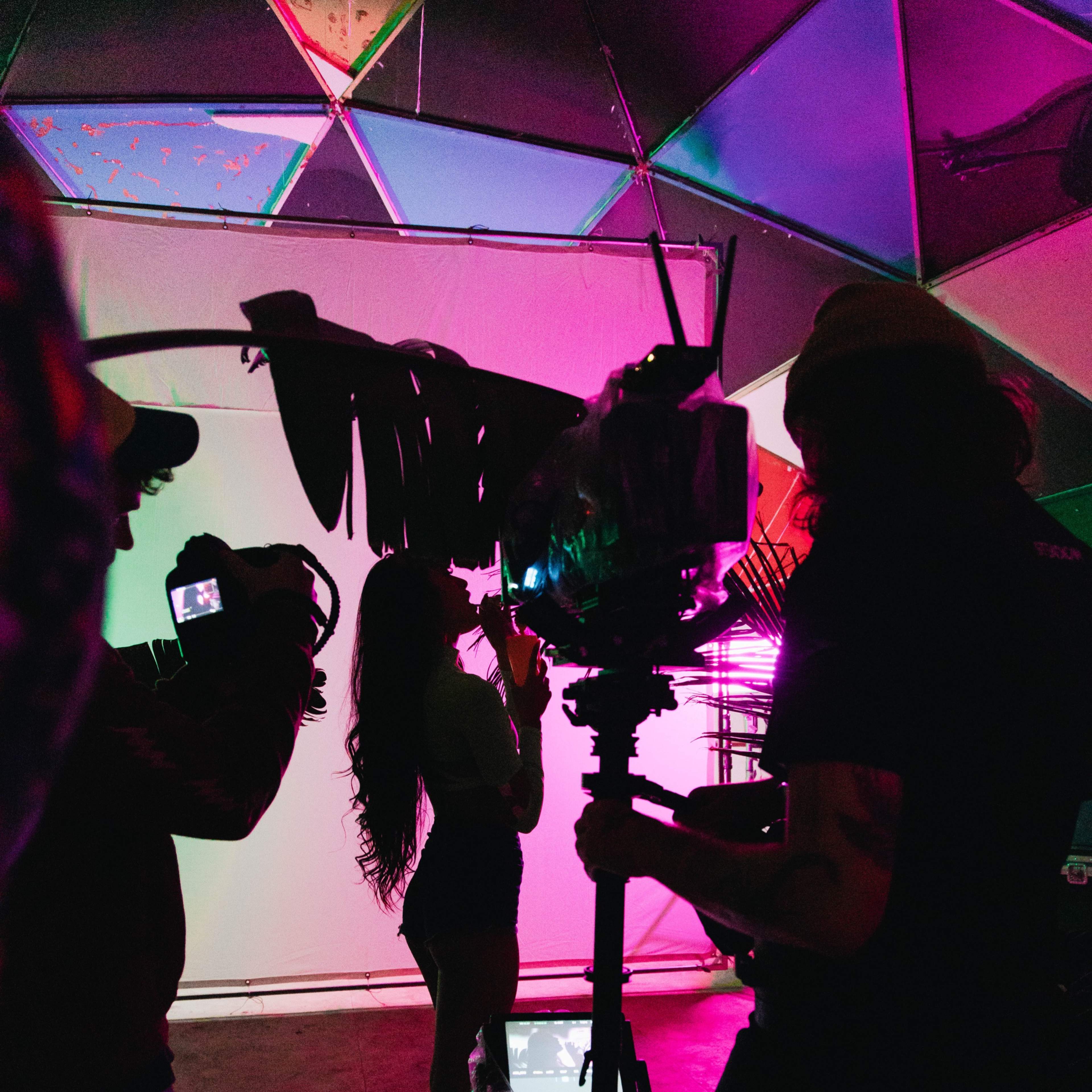 A film crew is shooting a scene in a colorful, illuminated set with a camera mounted on a stabilizer.