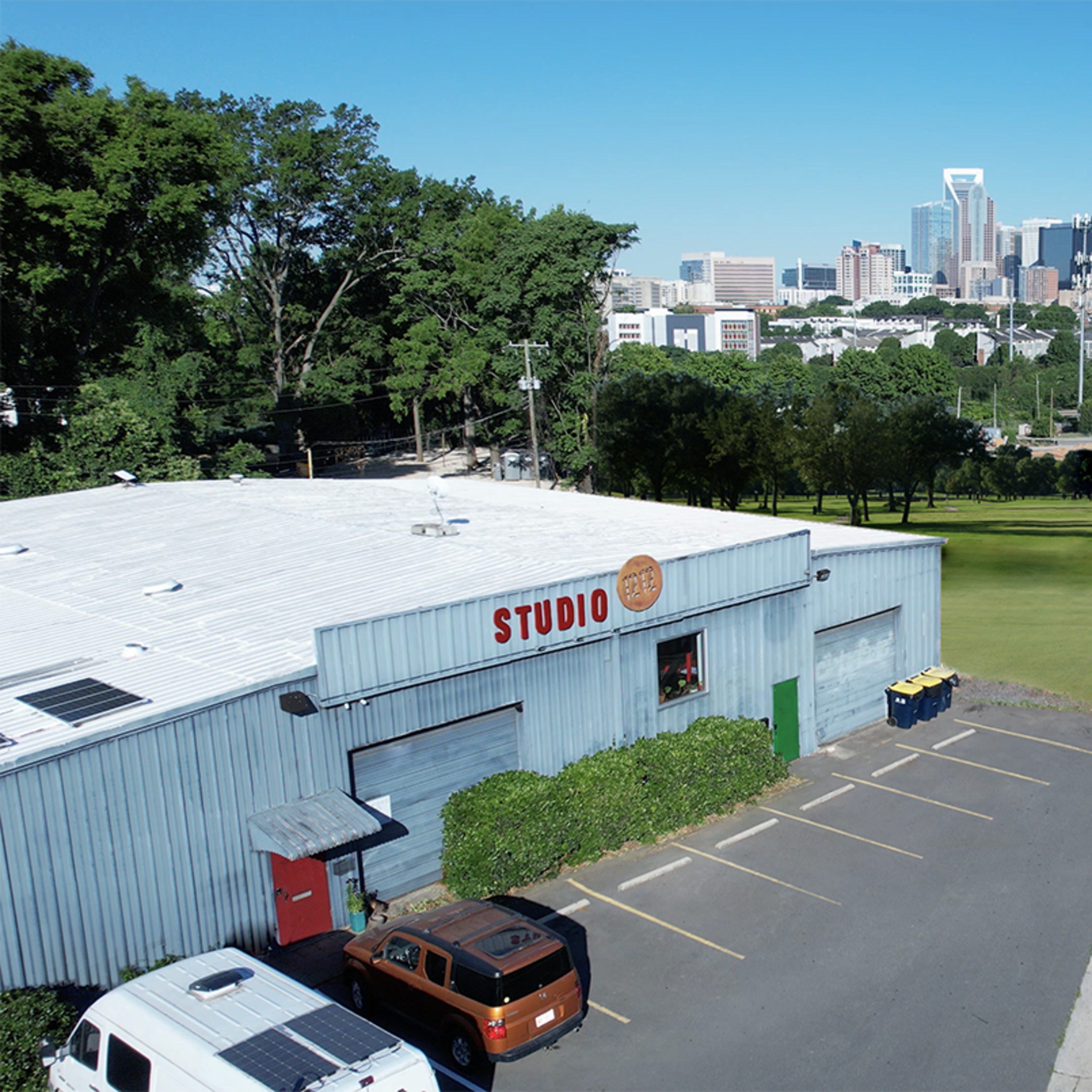 A parking area next to a building labeled "STUDIO," with a clear view of a city skyline in the background and a road running alongside.
