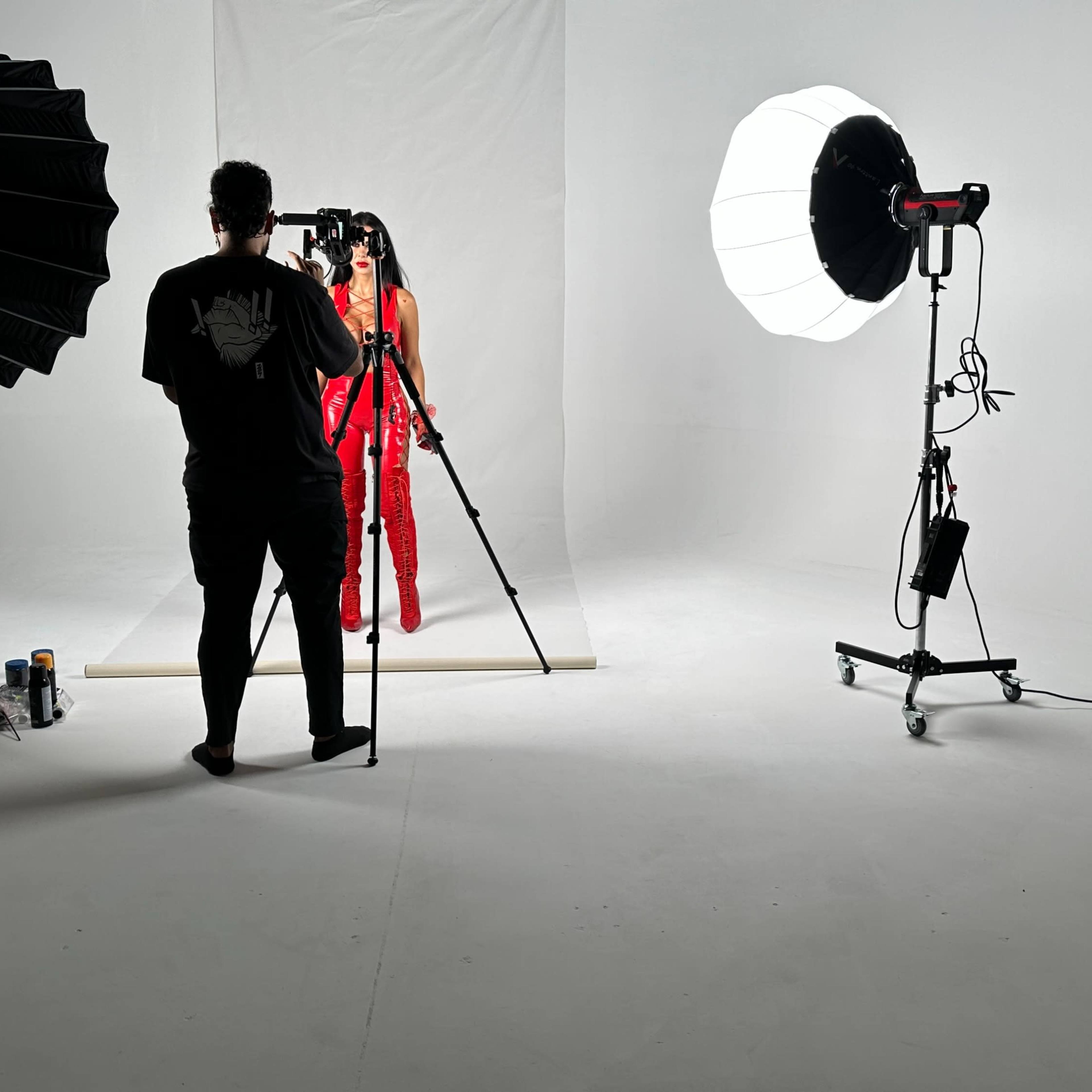 A photographer captures a model dressed in red against a white backdrop, surrounded by professional lighting equipment.