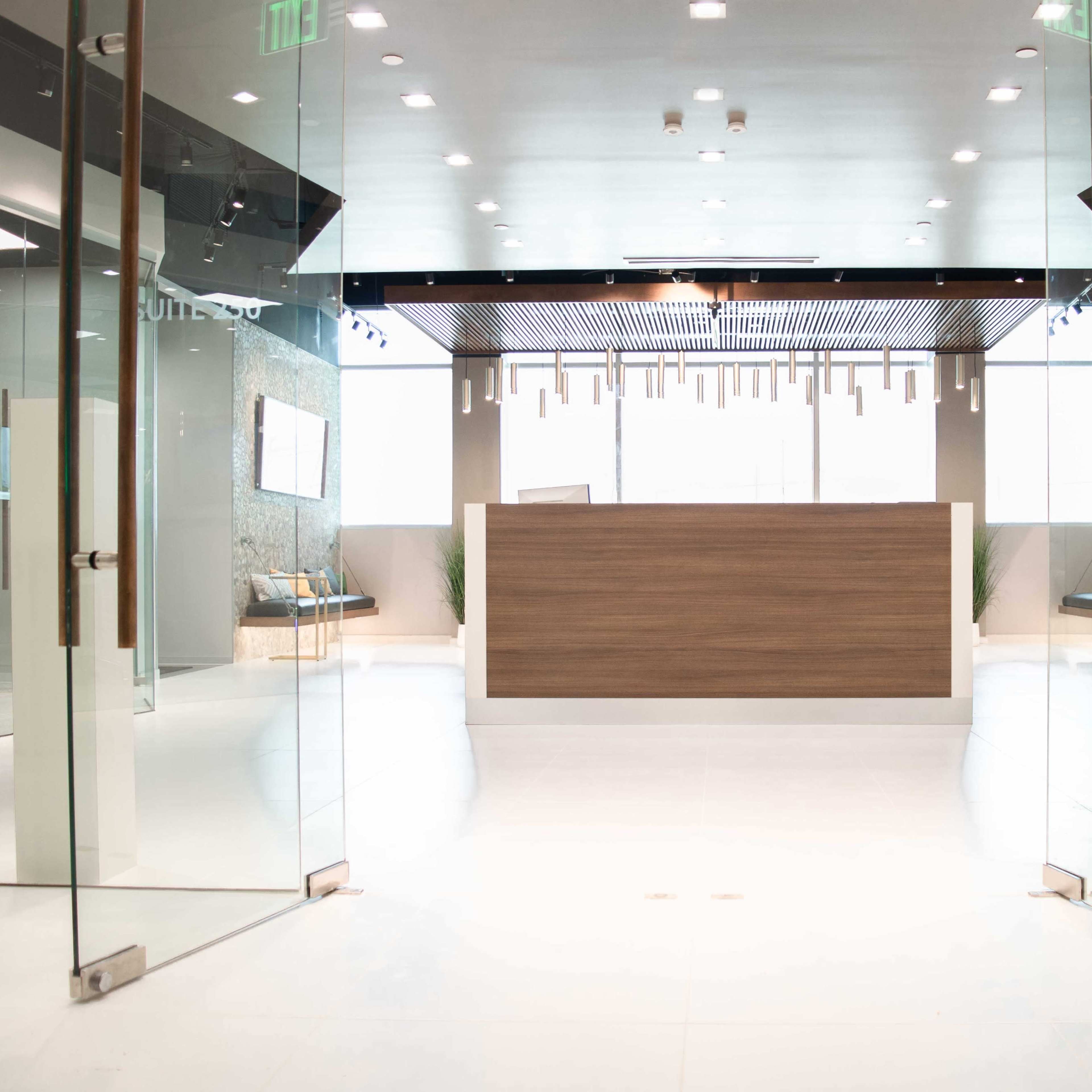 A modern reception area with a wooden front desk, glass doors, and minimalist decor.