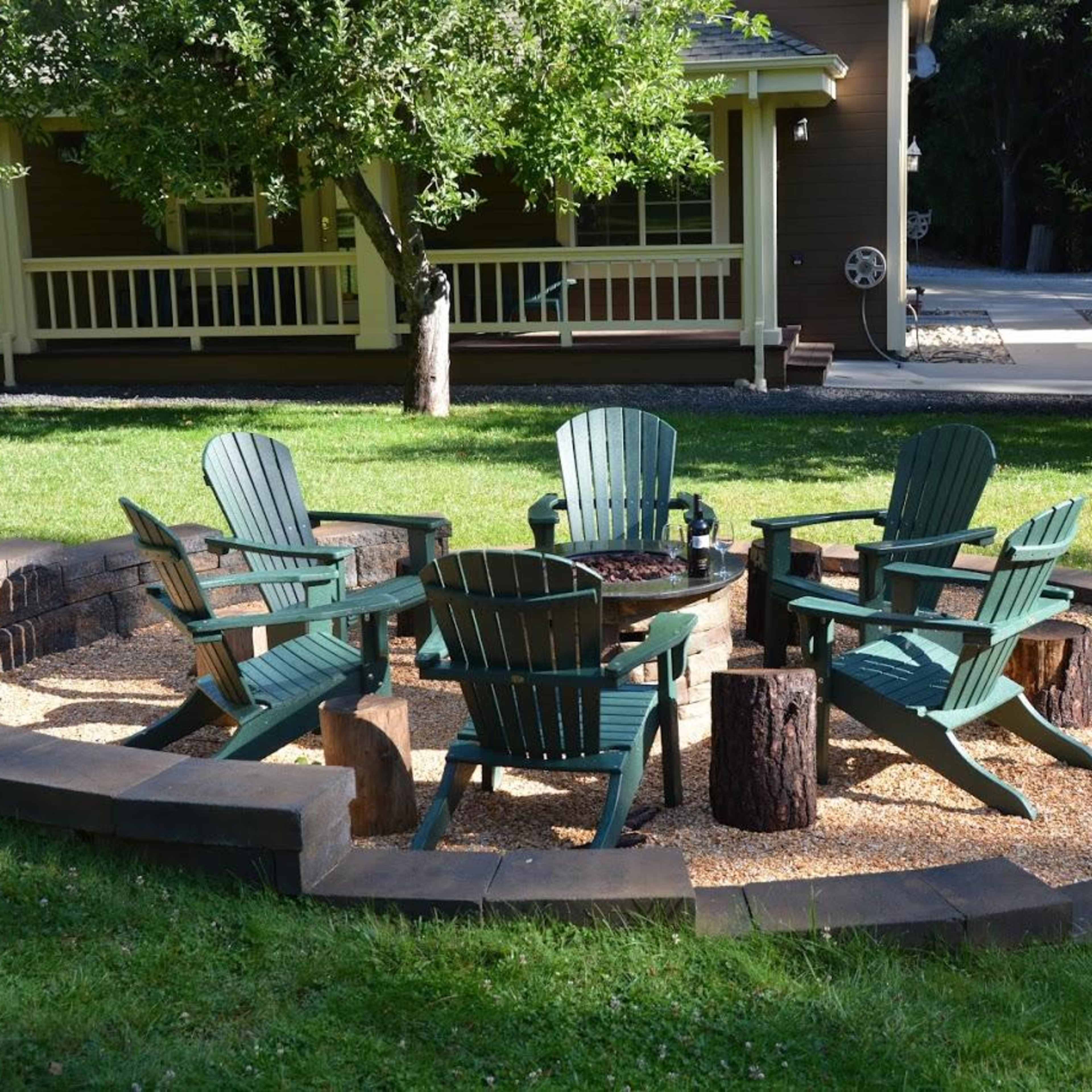 A circular seating area with wooden chairs surrounds a fire pit, surrounded by gravel and bordered by stone.