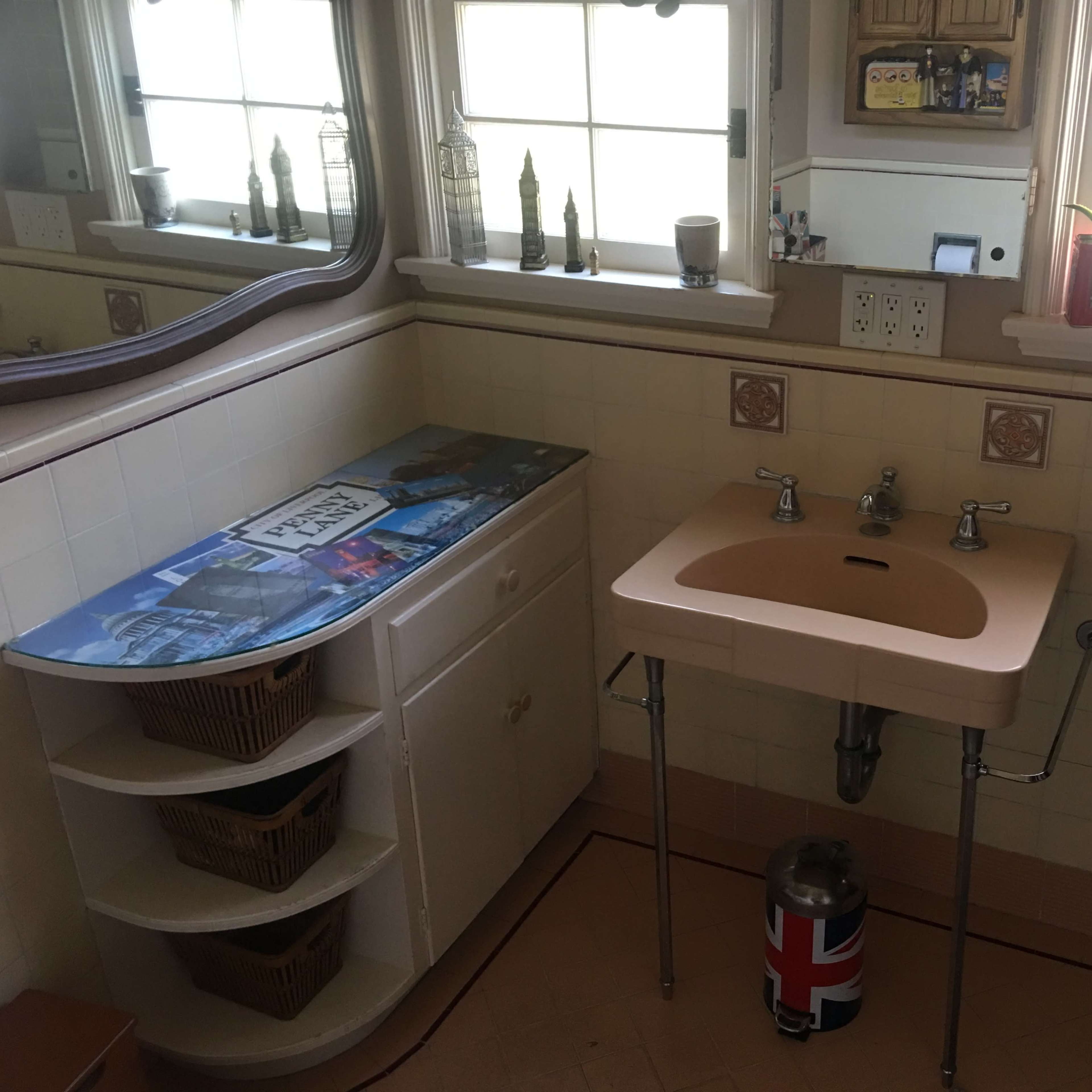 A bathroom with a unique peach-colored sink, storage cabinets with wicker baskets, and multiple mirrors reflecting the light from a window.