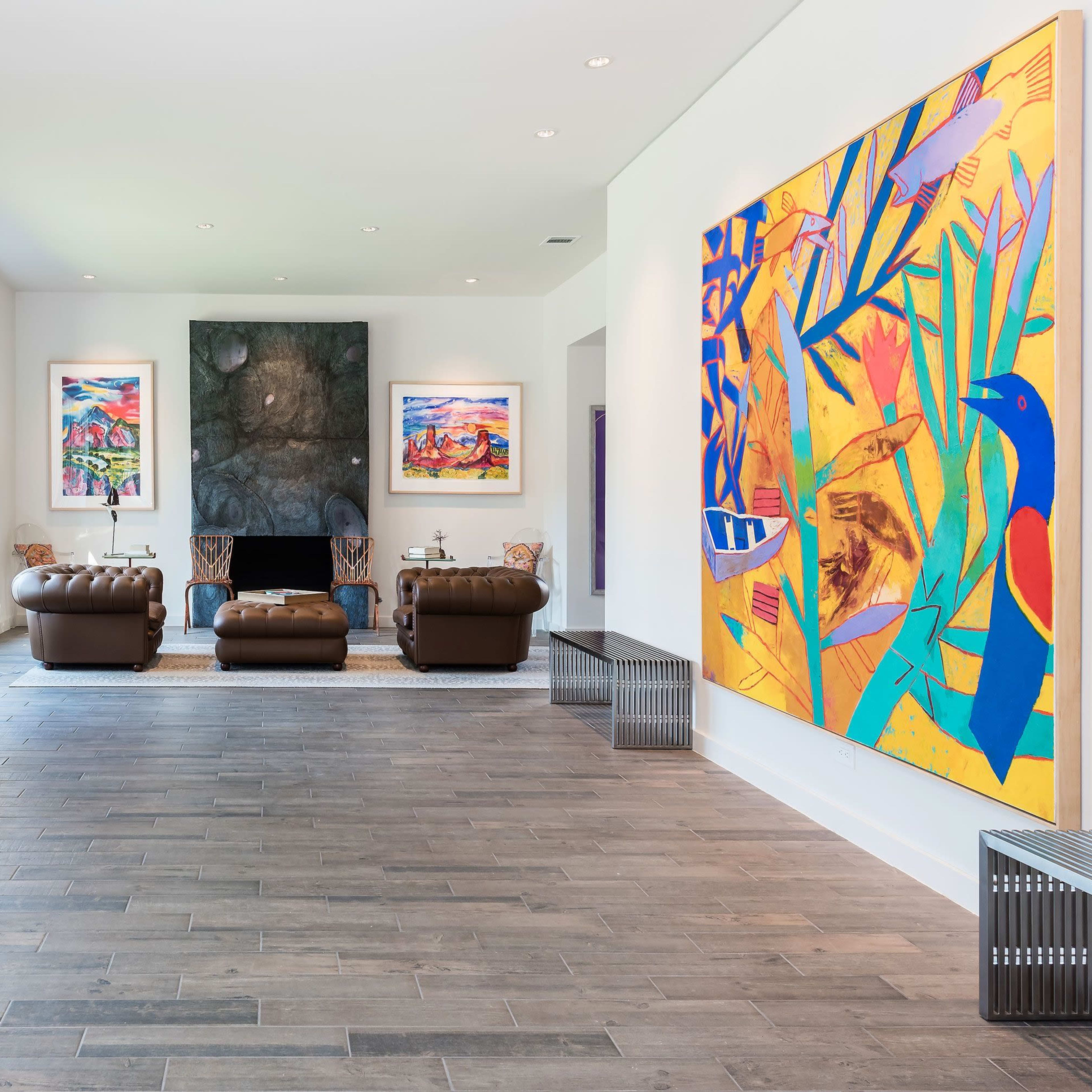 A bright living room featuring modern artwork on the walls, a fireplace, and brown leather sofas arranged around a central rug.