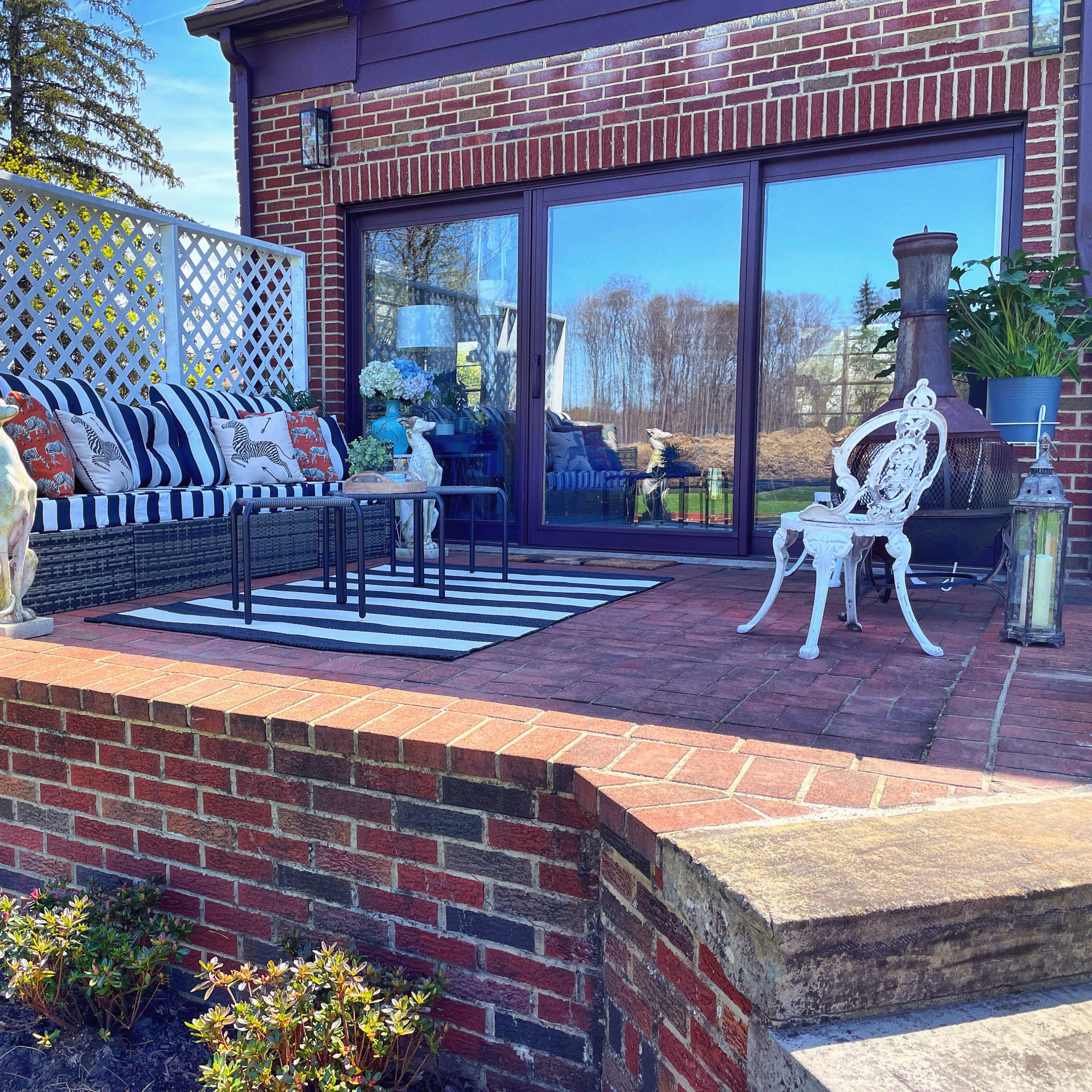 A patio area with a striped outdoor rug, a seating arrangement featuring cushions, and decorative elements against a brick wall.