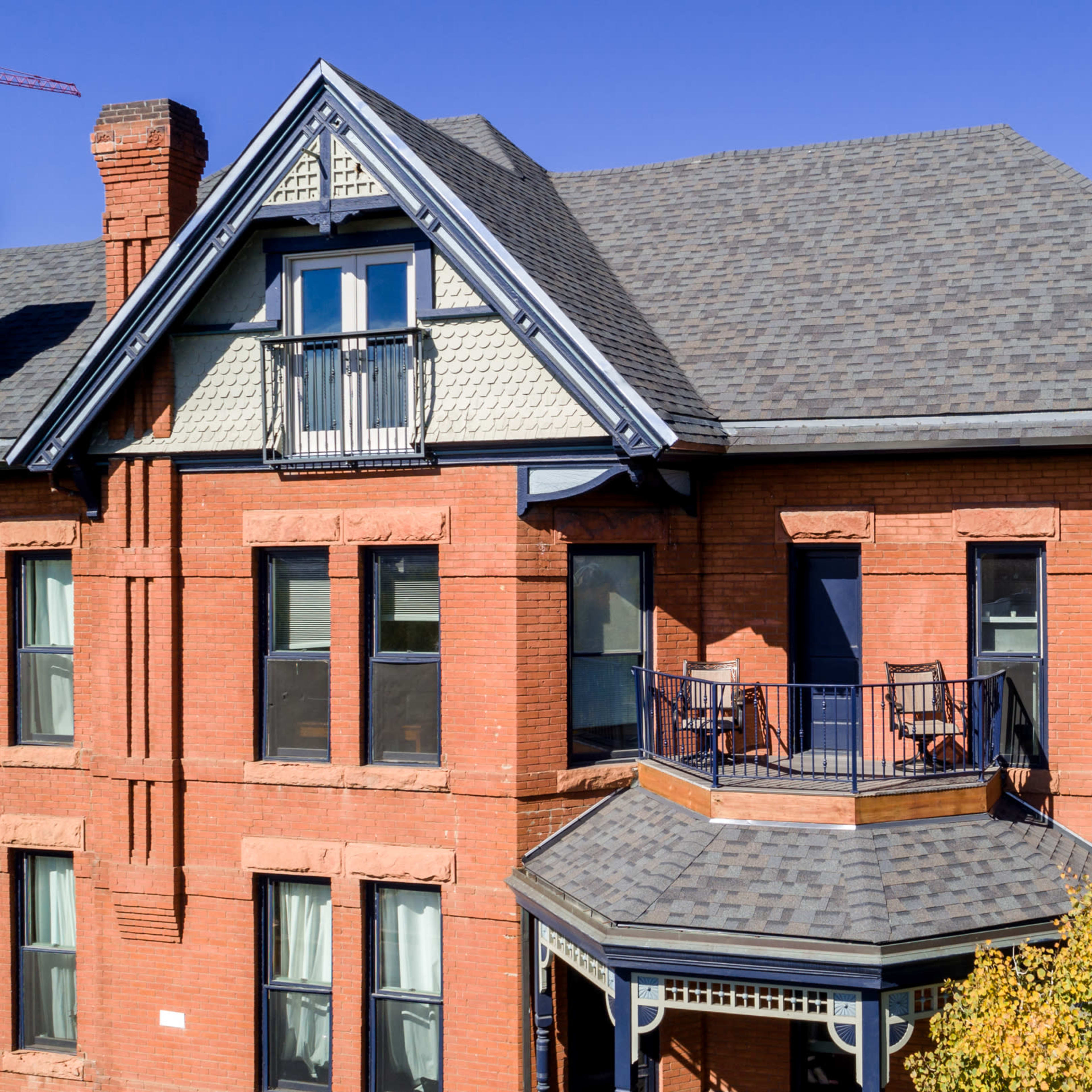 A red brick building with a steep roof, featuring a balcony and multiple windows, set against a clear blue sky.