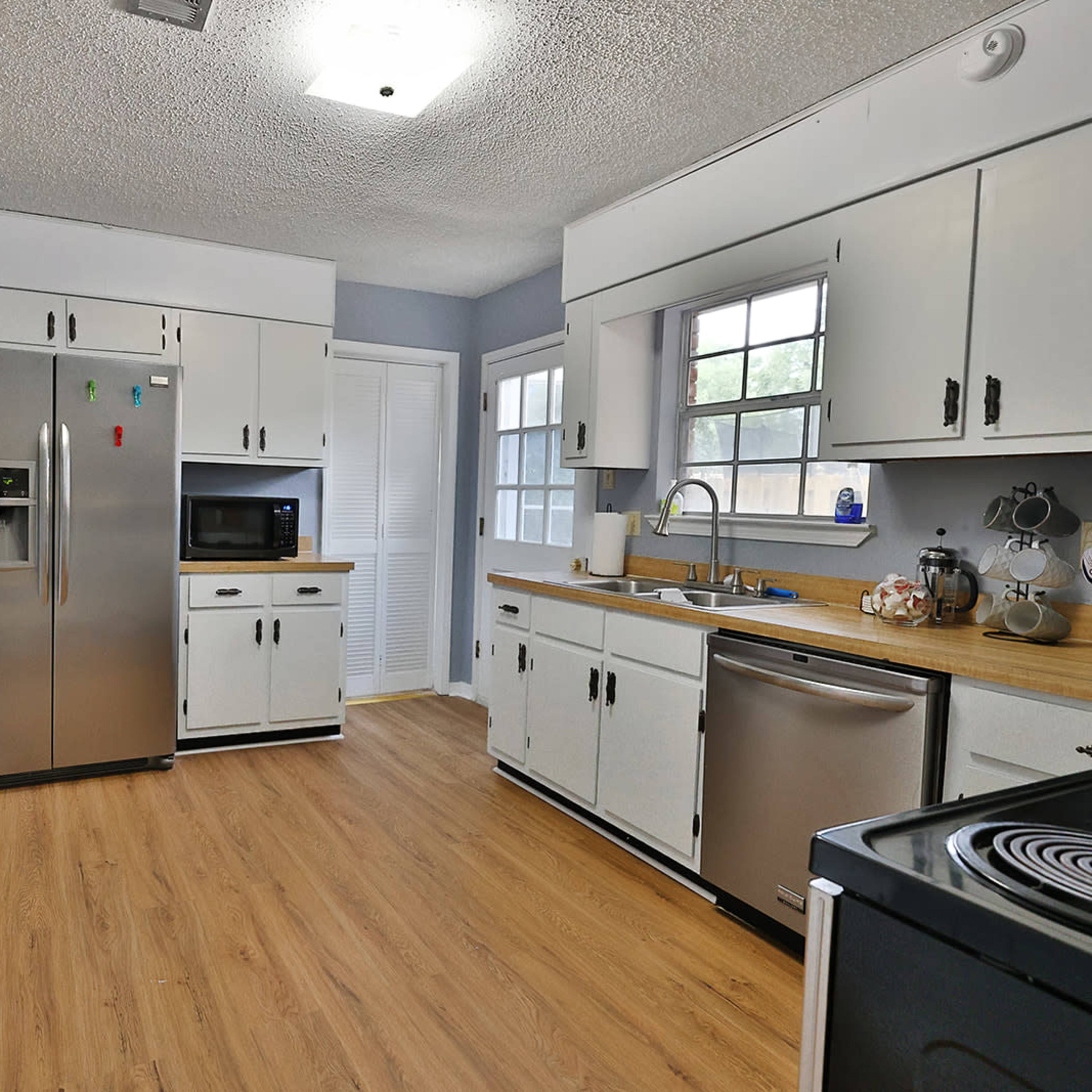 A kitchen with stainless steel appliances, white cabinets, and a wood countertop, featuring a window and a door leading to an outdoor area.