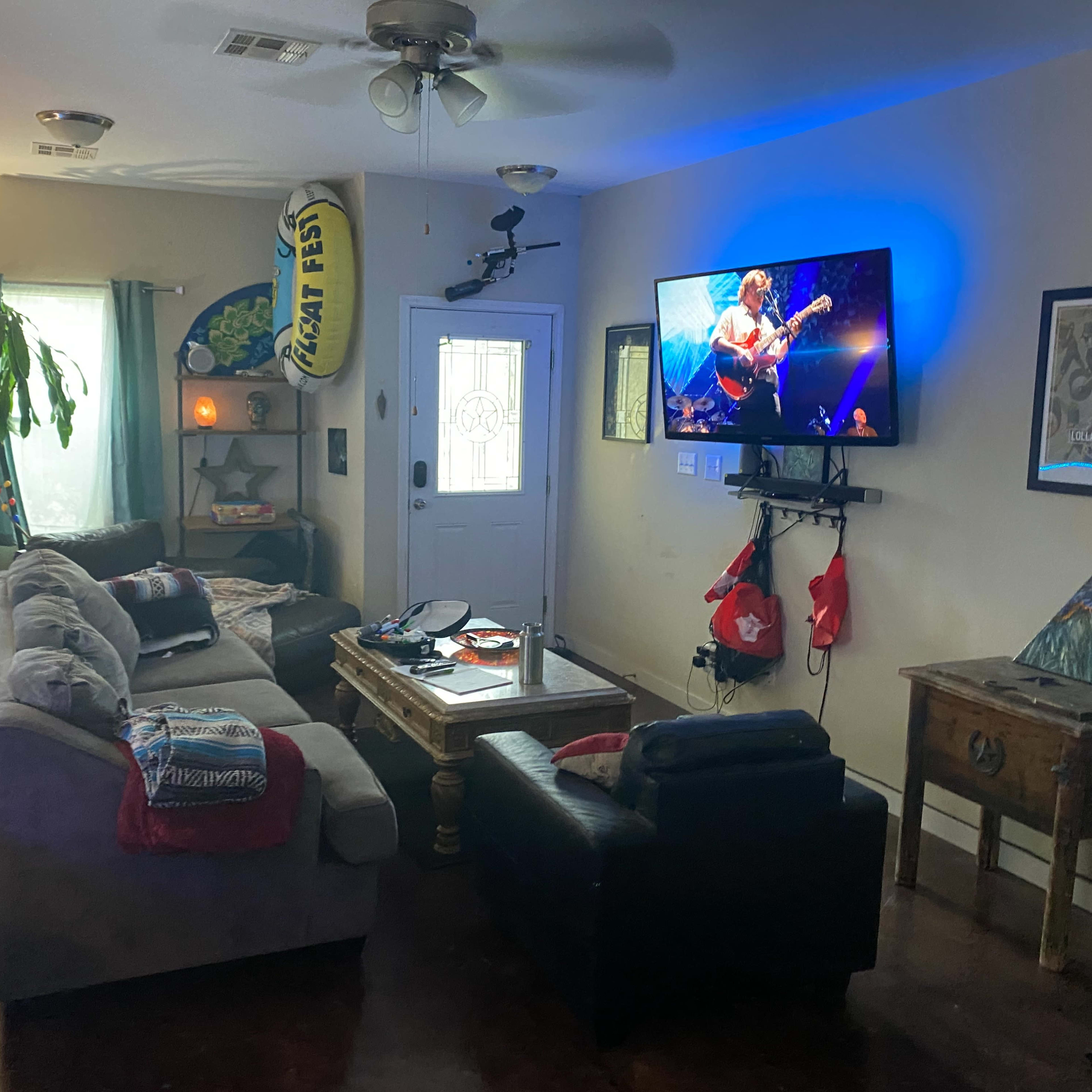 The living room features a sectional sofa, a coffee table, a TV displaying a musical performance, and various decor items.