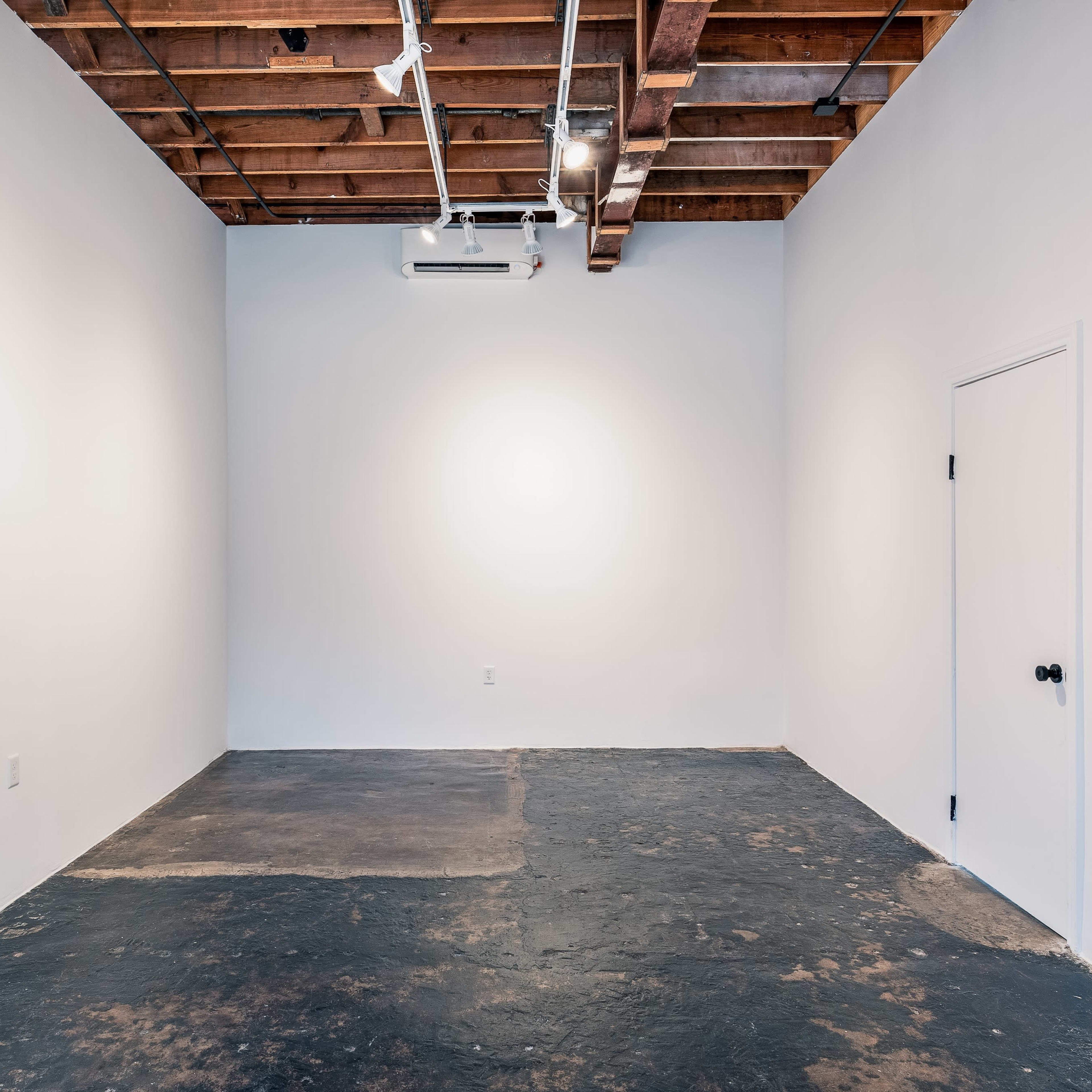 An empty room with a concrete floor, white walls, and exposed wooden beams on the ceiling.