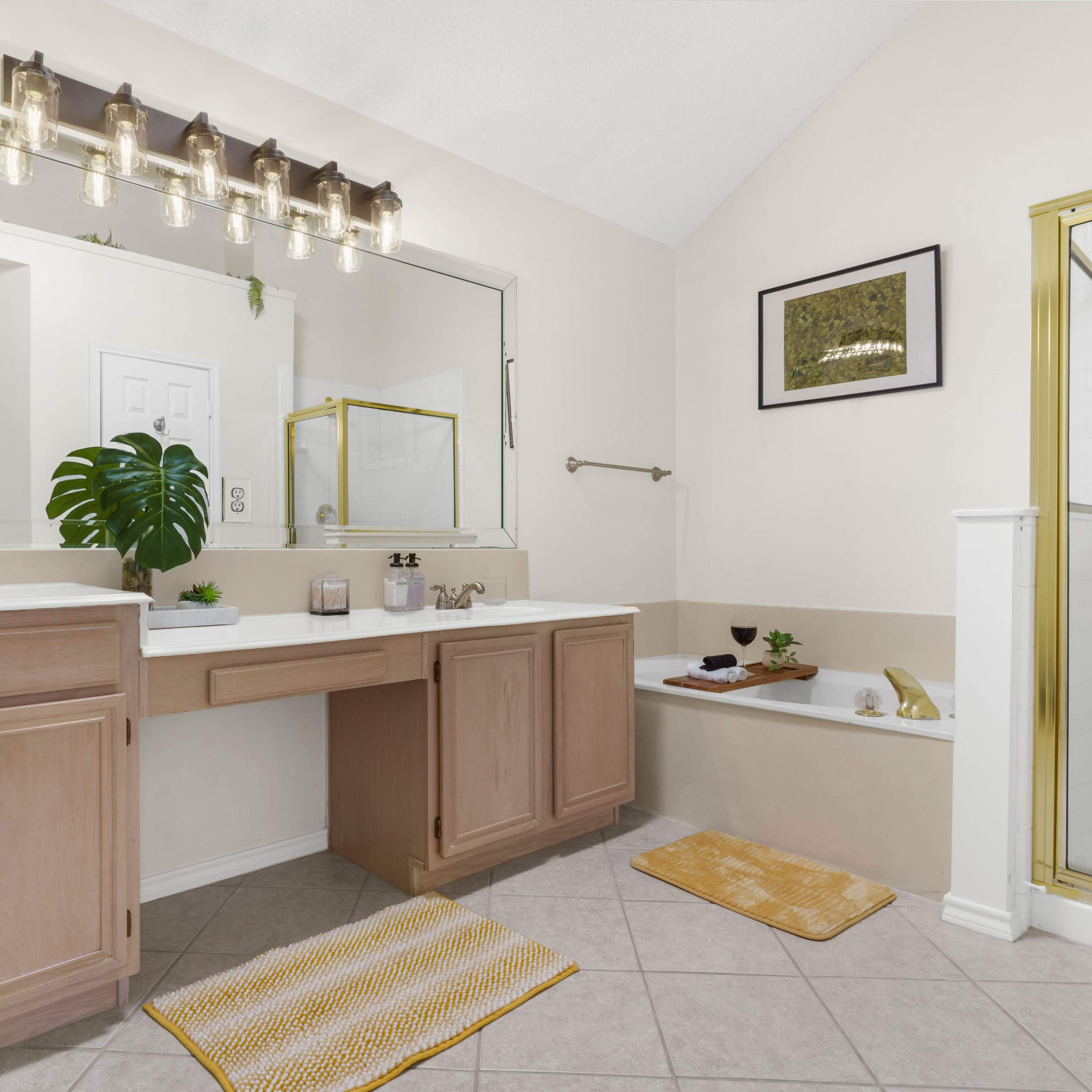 A well-lit bathroom featuring a double vanity with wooden cabinets, a large mirror, and a shower stall beside a bathtub.