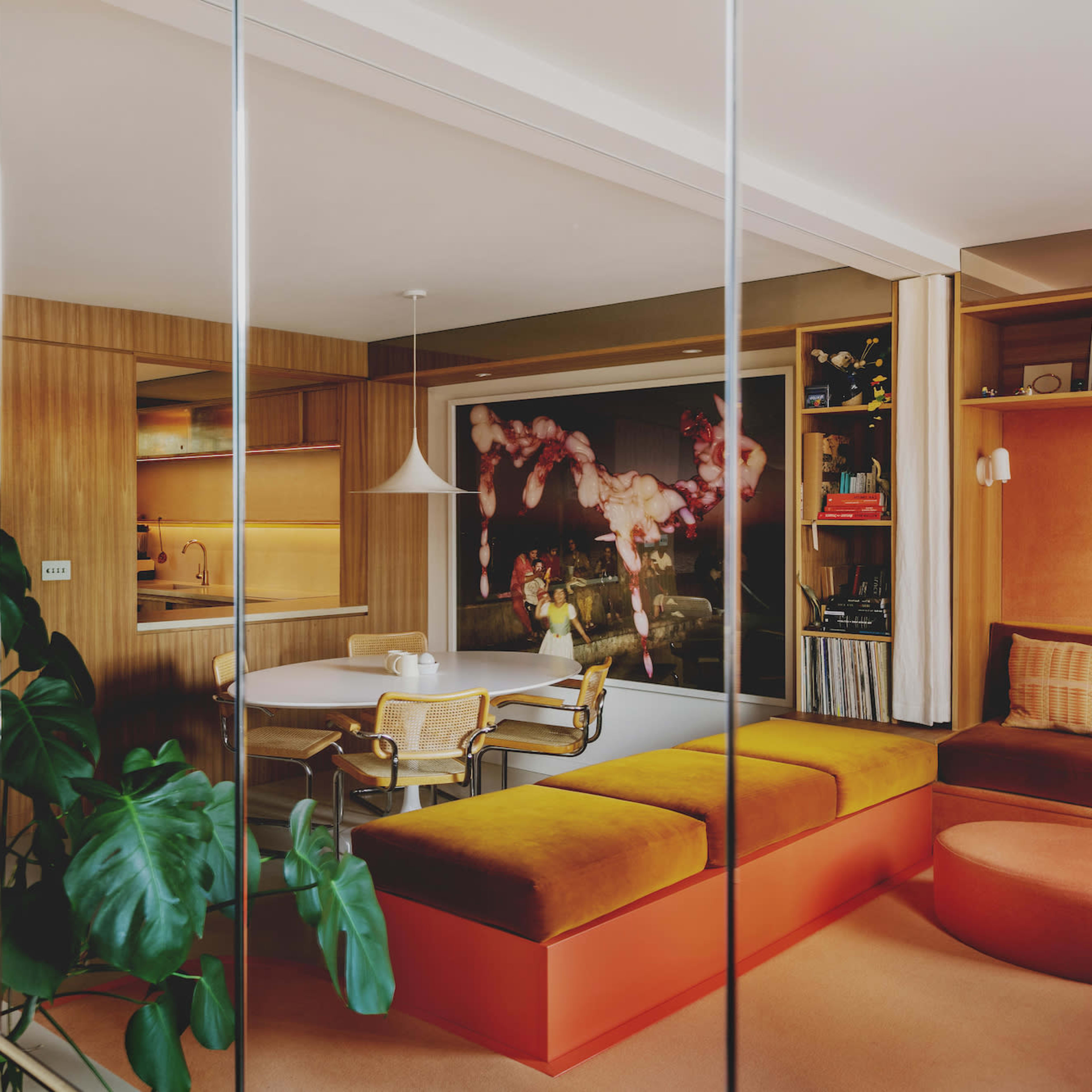 A modern interior space featuring a staircase, a kitchen area, and seating with large plants and vibrant decor.