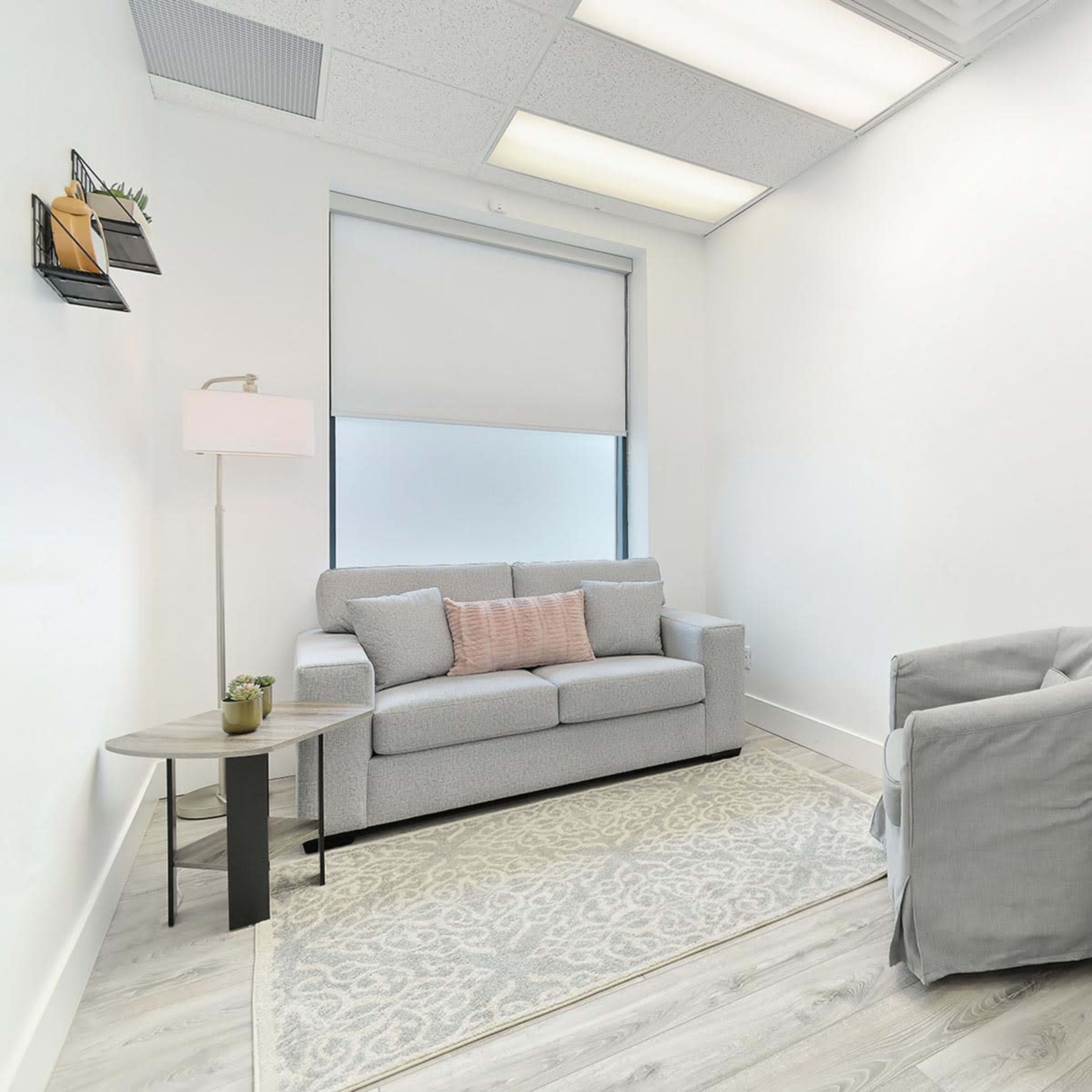 A small, neatly arranged office space with a couch, a side table, a desk, and a chair.