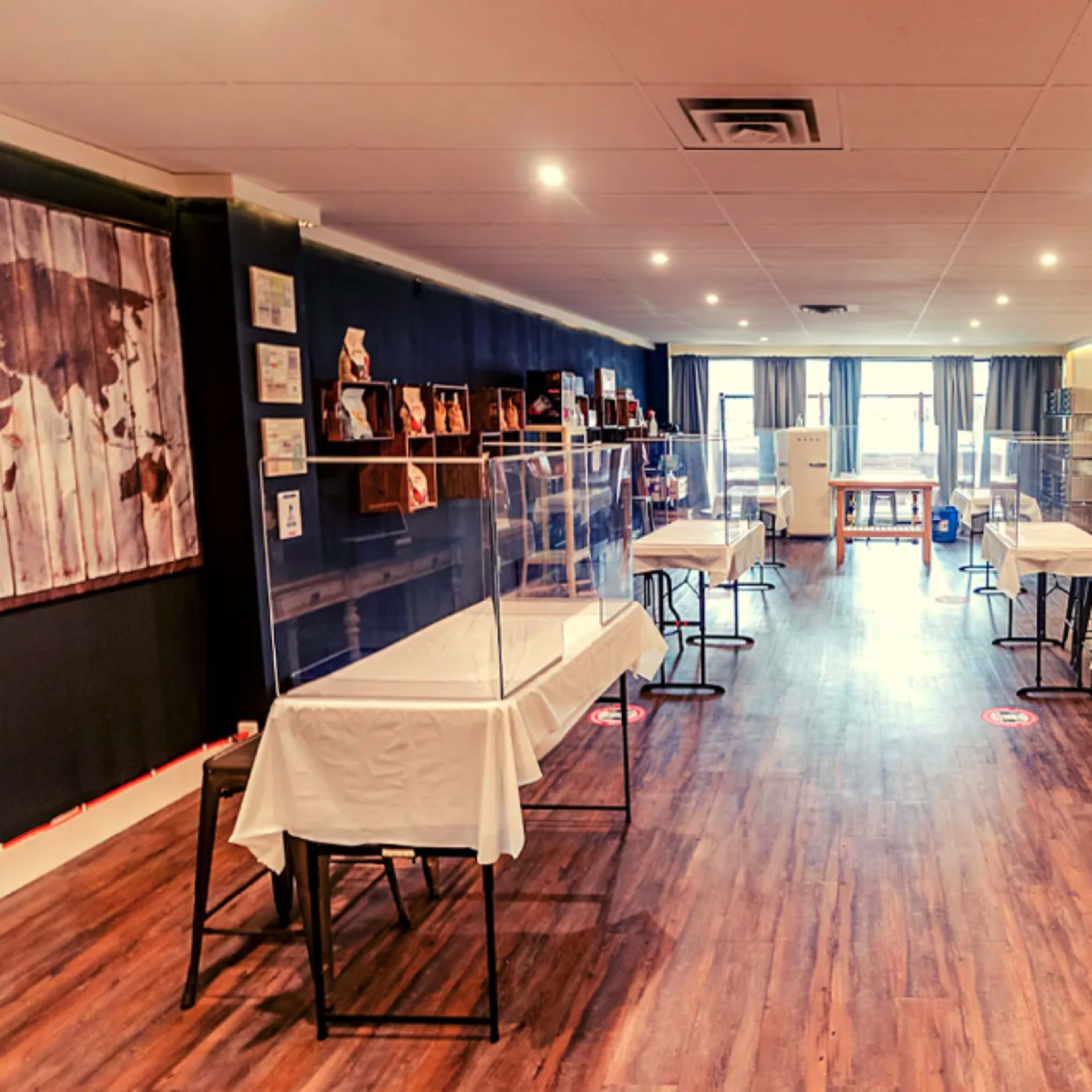 A spacious room with several tables covered in white cloth, each enclosed by clear plastic barriers, creating separate workstations.