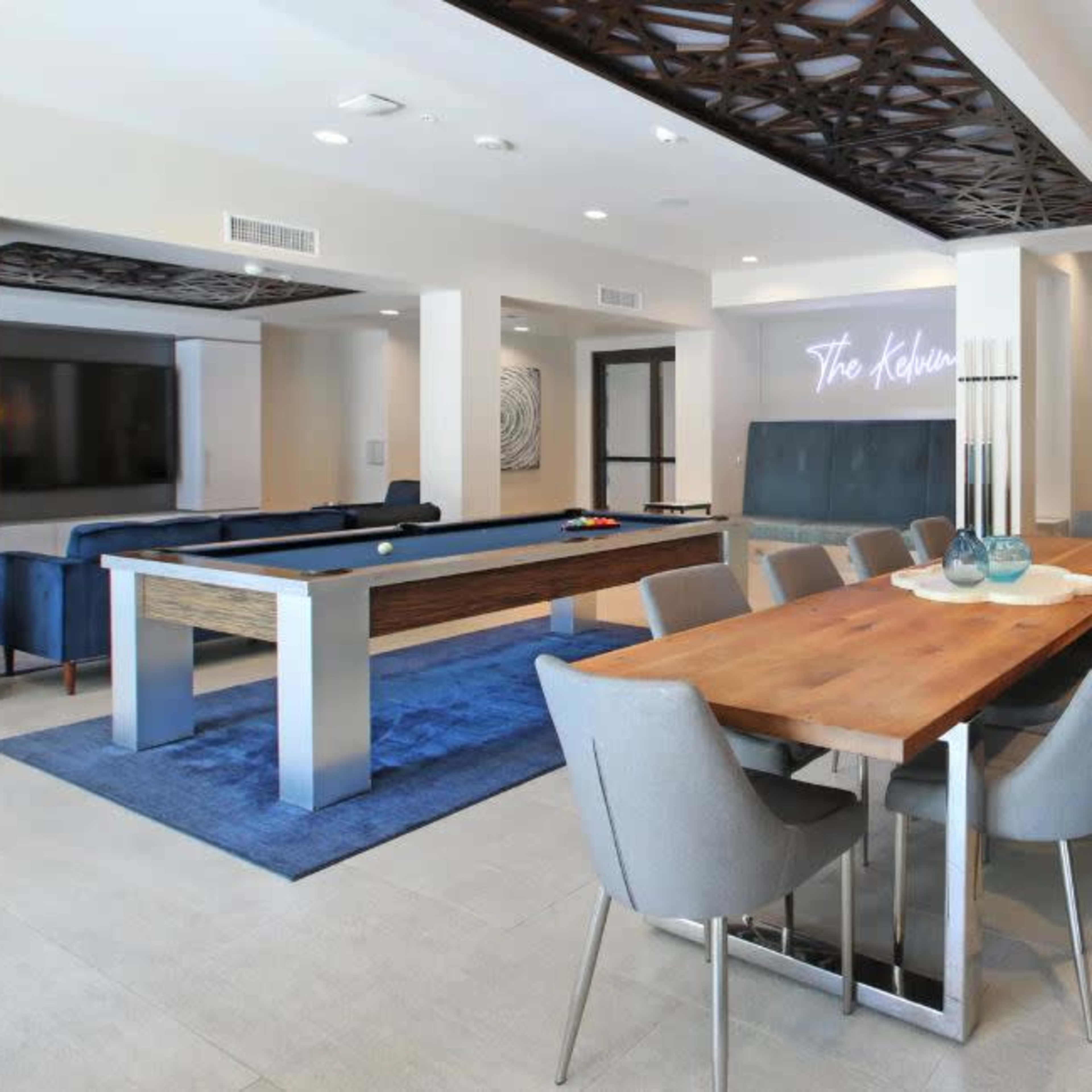 A modern communal space featuring a dining table, pool table, and a living area with couches and a television.