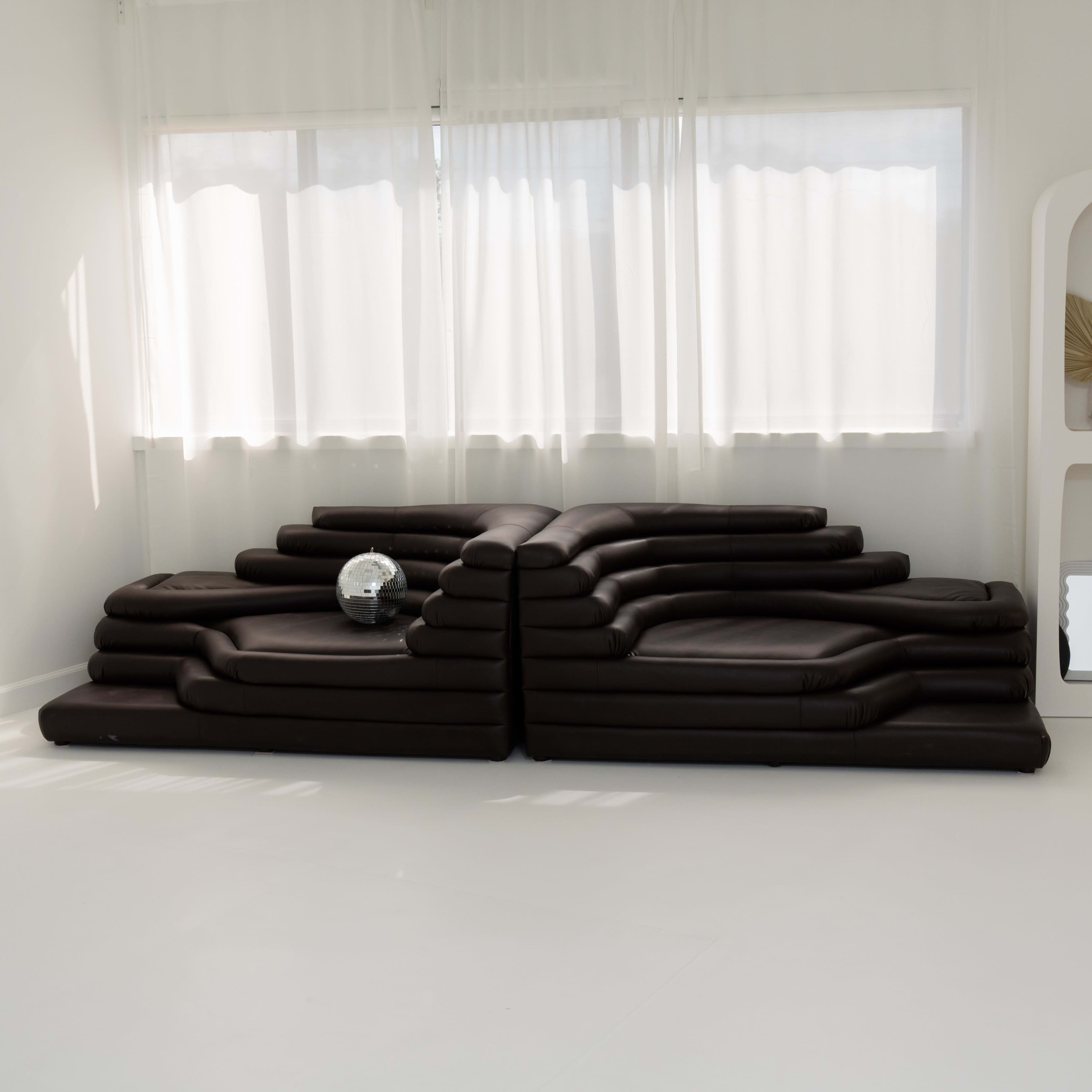 A modern, minimalist lounge area with a unique, sculptural sofa arrangement and a decorative glass ball on a side table.