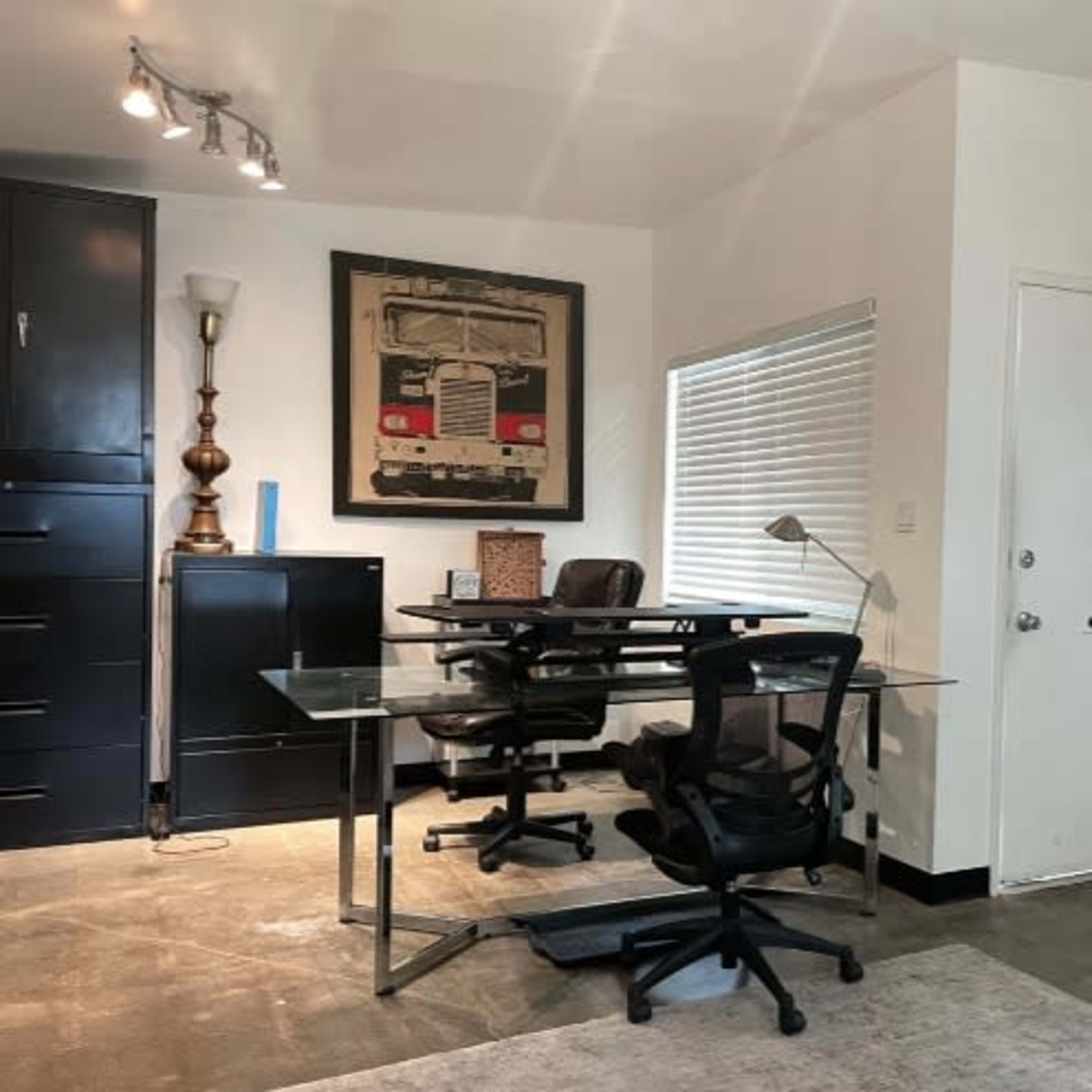 A modern office space with two black office chairs, a glass desk, a large black storage cabinet, and a wall-mounted chalkboard.