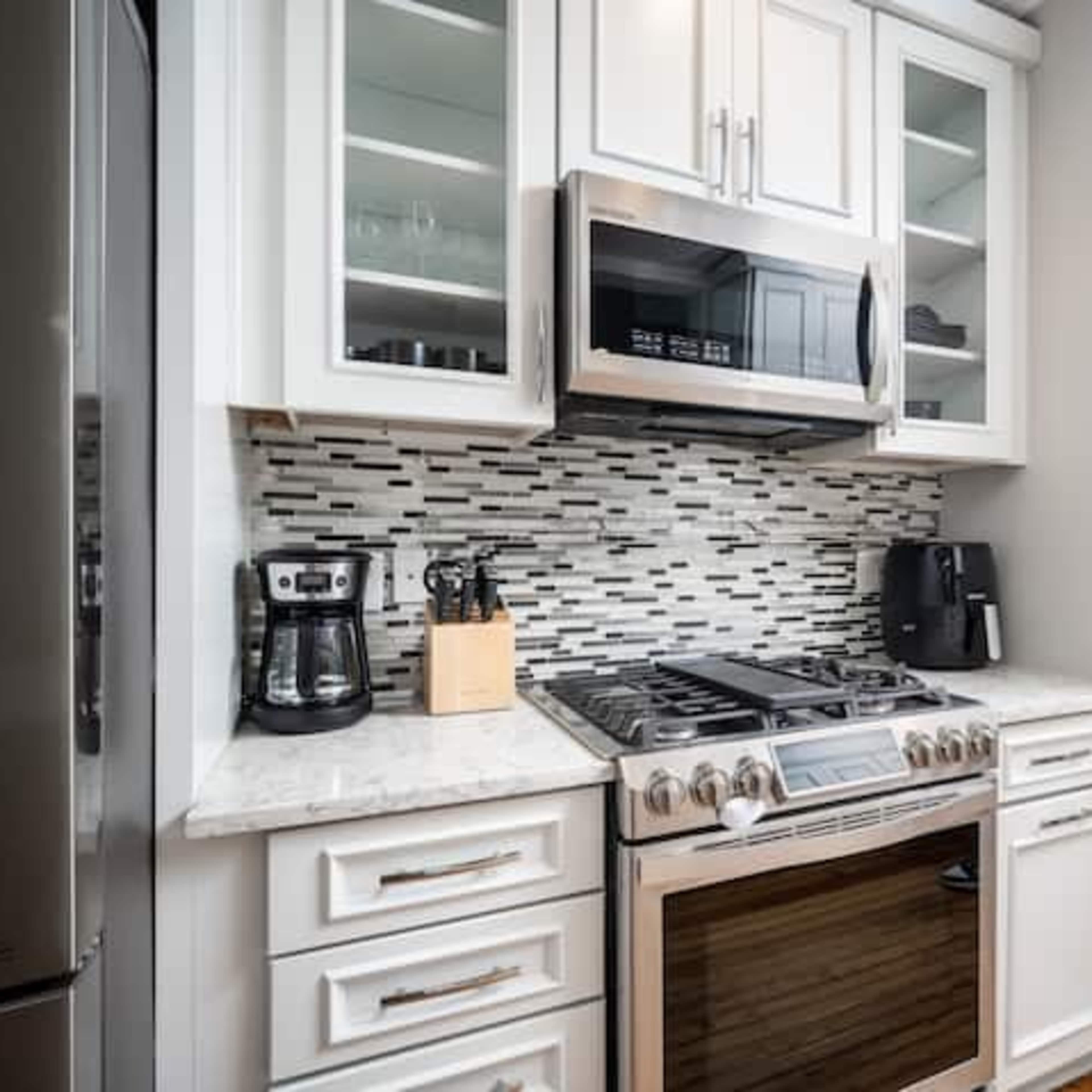 A modern kitchen with white cabinetry, a stainless steel microwave, and a gas stove beneath a tiled backsplash.