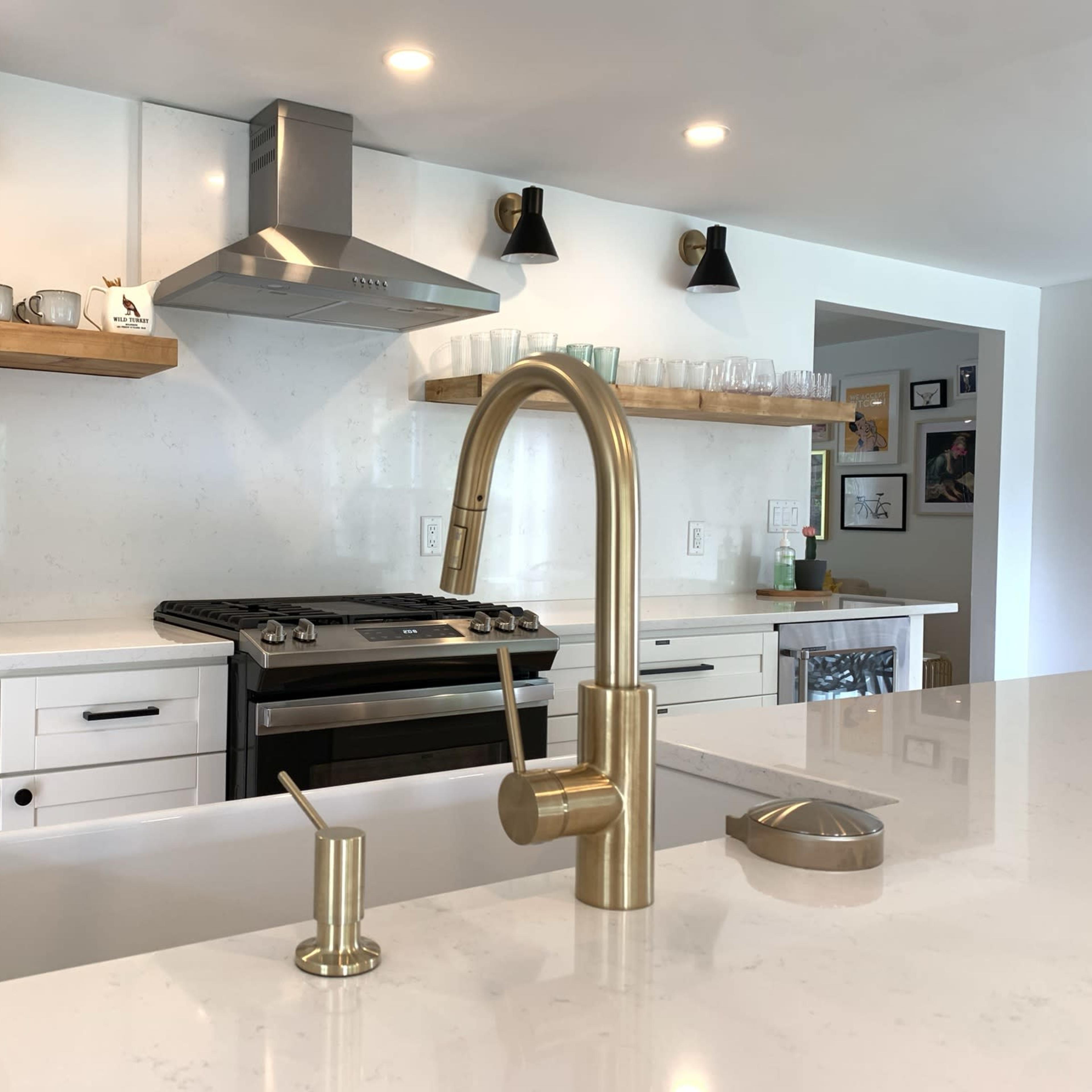 A modern kitchen with a stainless steel oven, a brass faucet, and open shelves displaying cups and glasses.