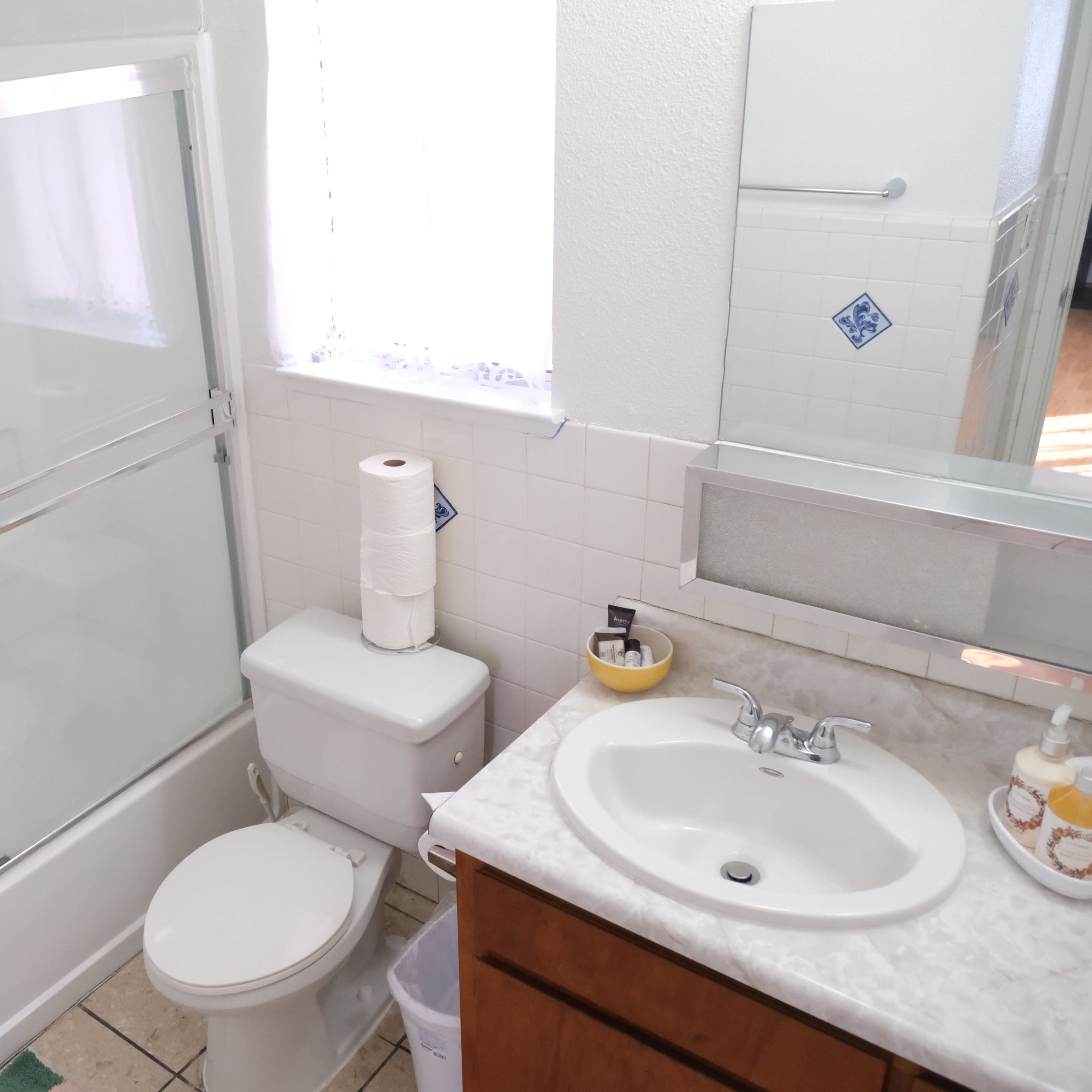 A bathroom with a shower, toilet, and sink, featuring white tiles and a wooden vanity.
