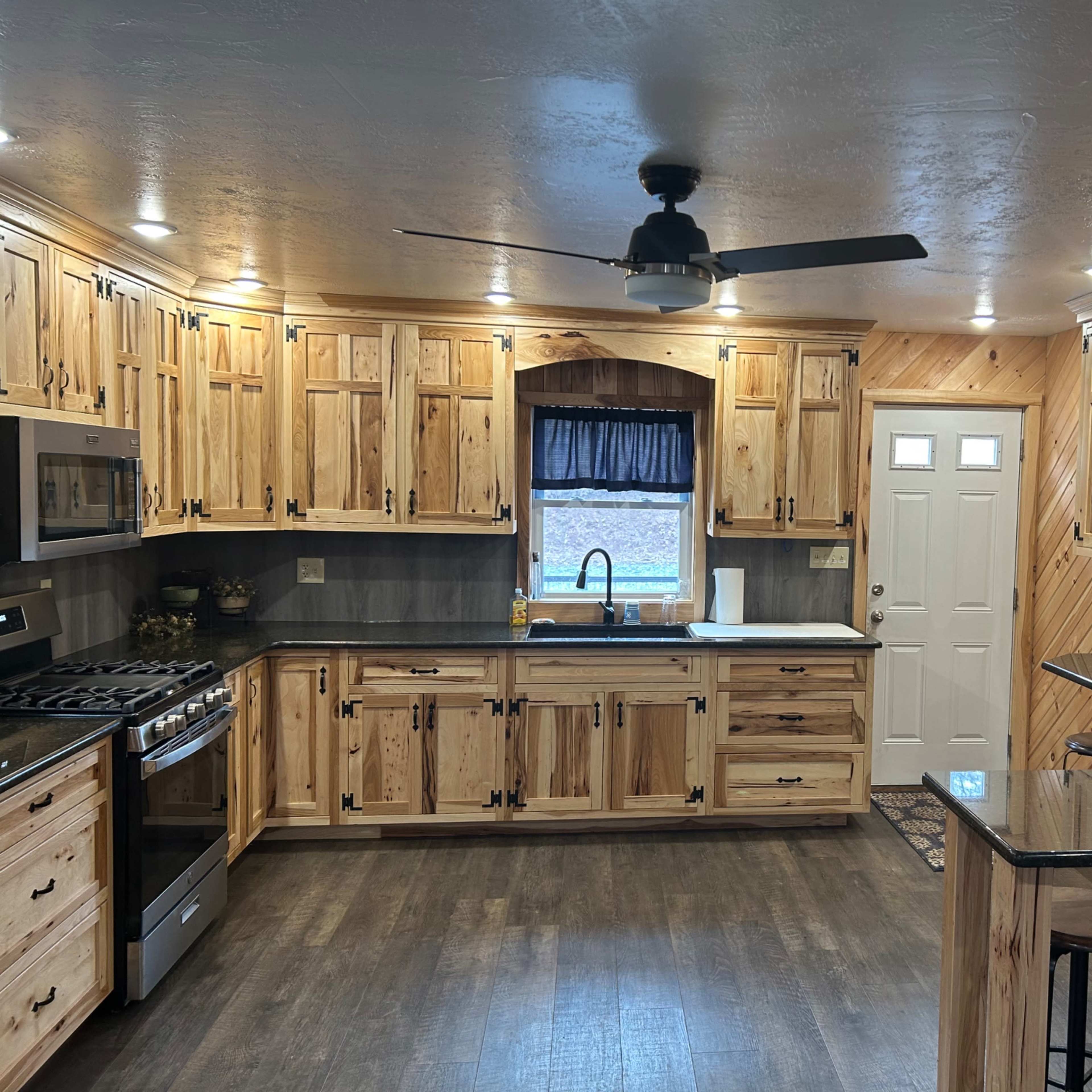 The kitchen features wooden cabinets, a ceiling fan, a stainless steel stove, and a small bar area with stools.