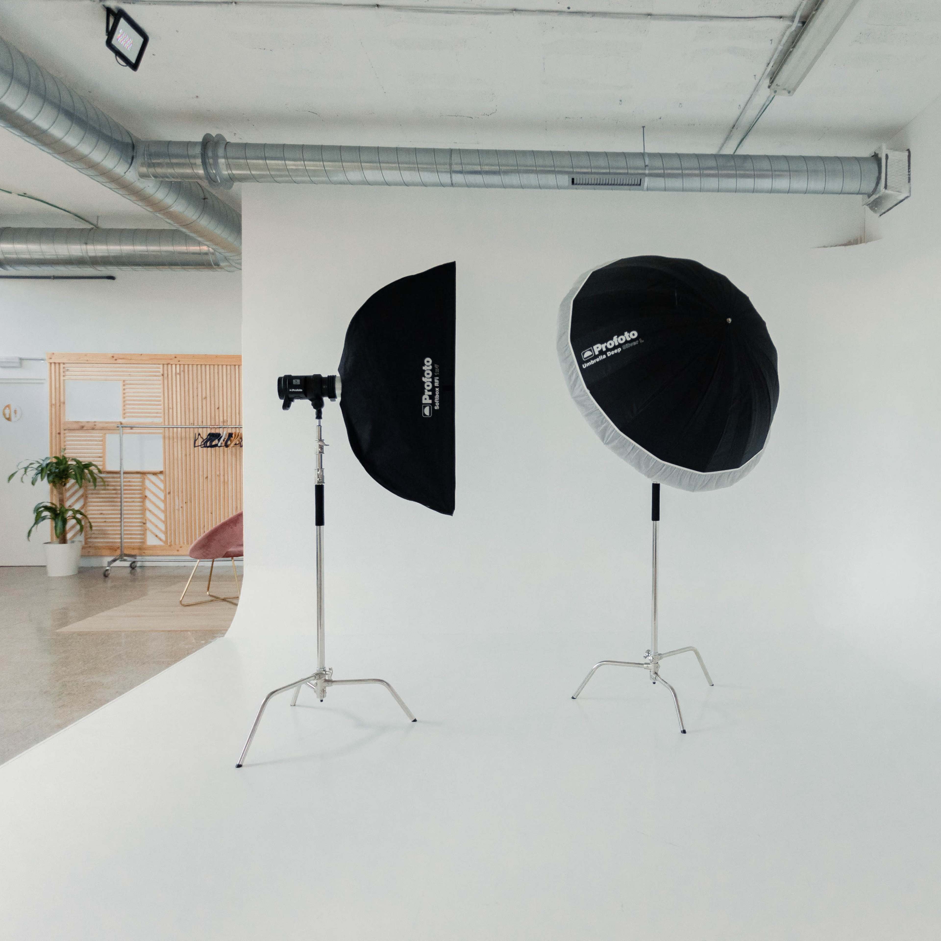 A brightly lit photography studio featuring two light umbrellas on stands and a seamless white backdrop.