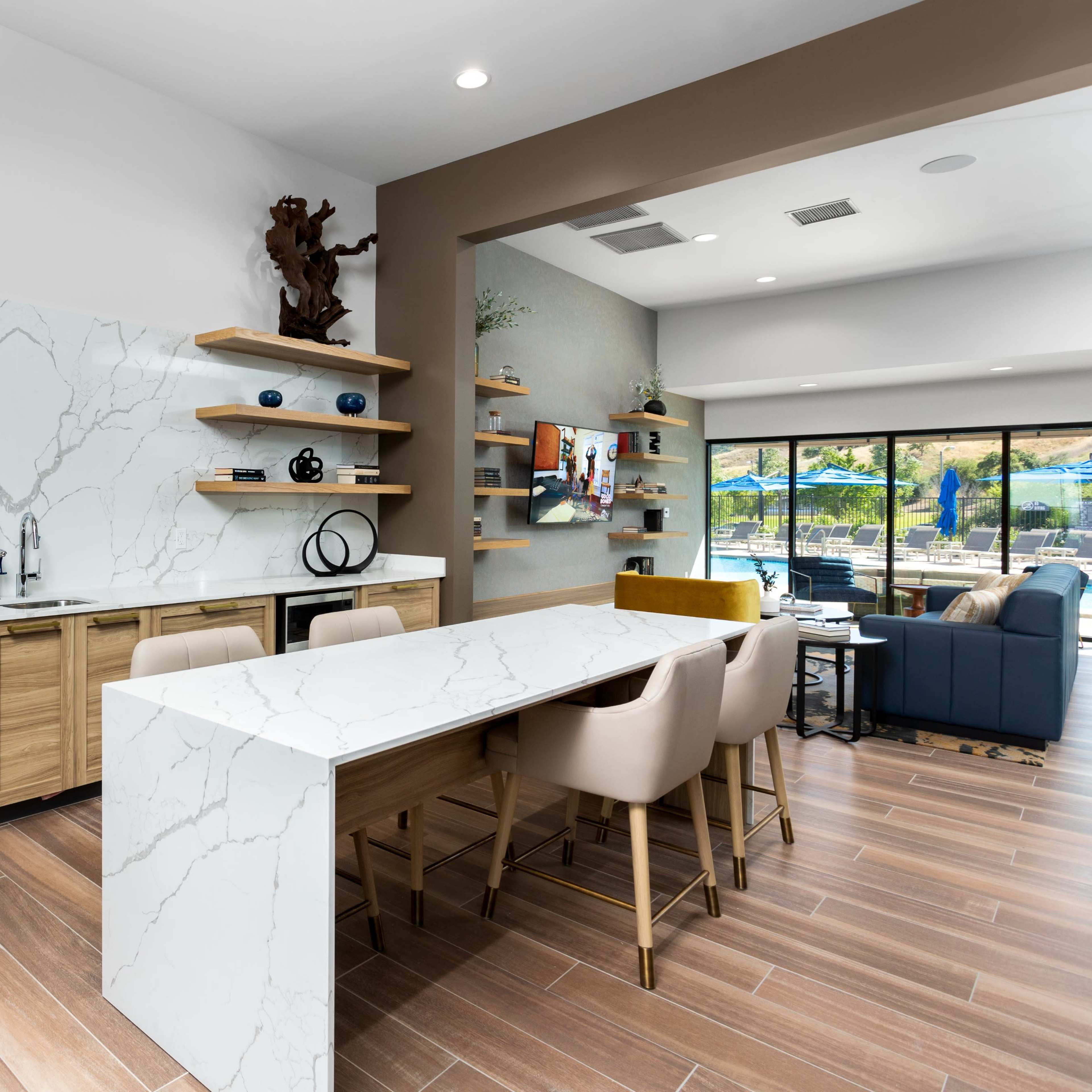 A modern kitchen with a large white marble countertop, wooden cabinets, and open shelving displaying decorative items.