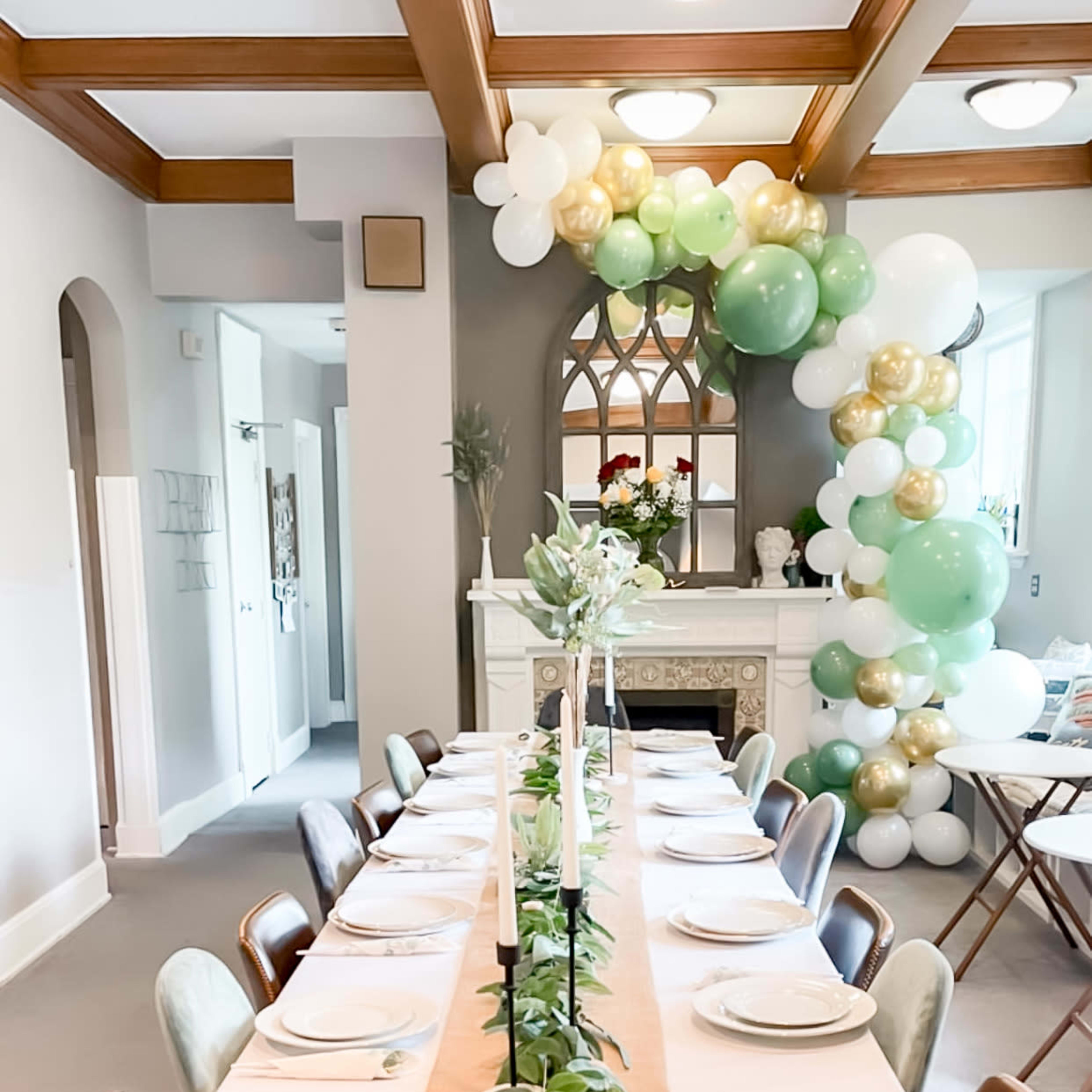 A dining table is elegantly set with plates and greenery, surrounded by decorative balloons, in a well-lit room.