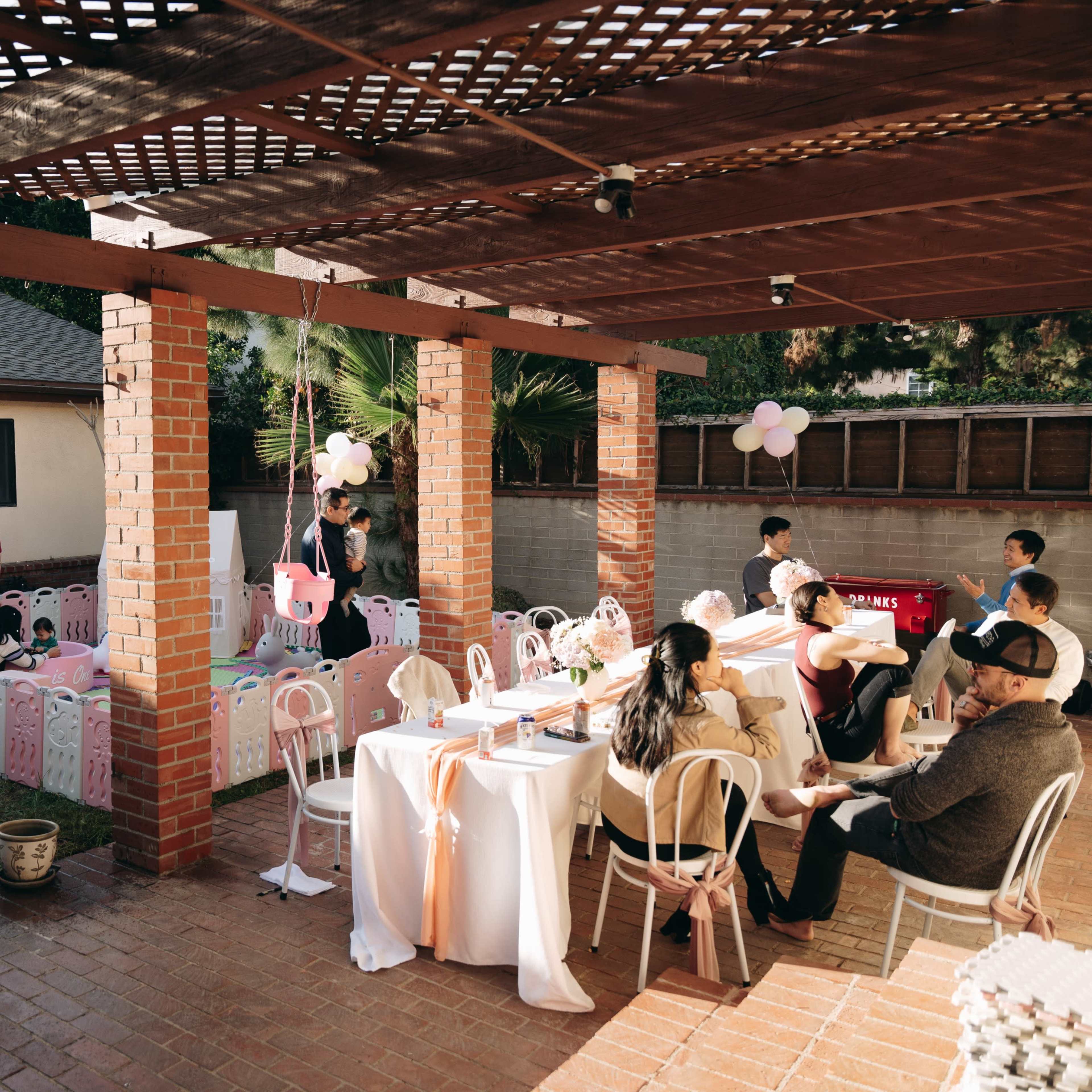 A backyard party is set up with tables and chairs, decorated with balloons, while guests engage in activities and conversations.