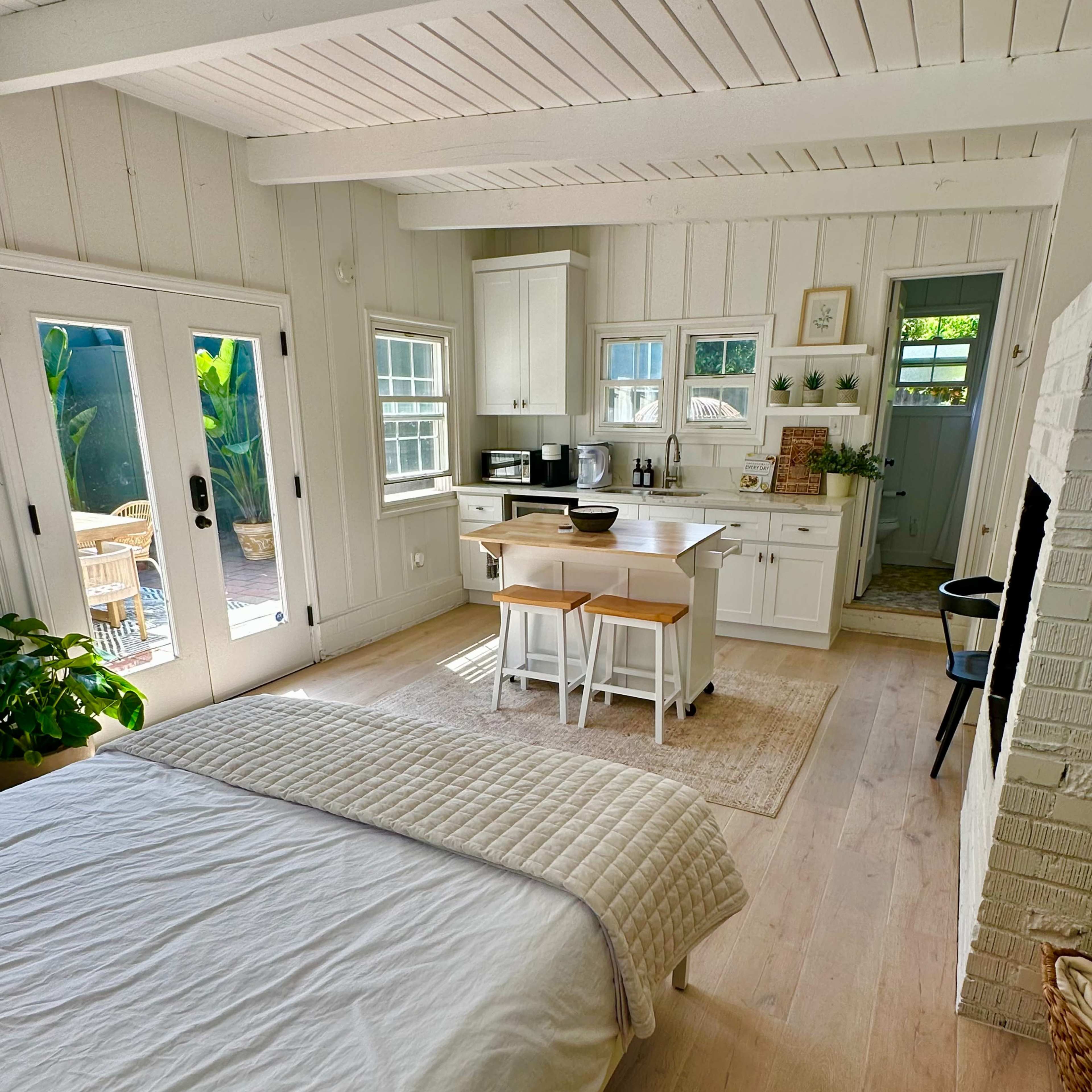 A bright, open-plan living space features a bedroom with a bed and a kitchenette area with a dining table and chairs.