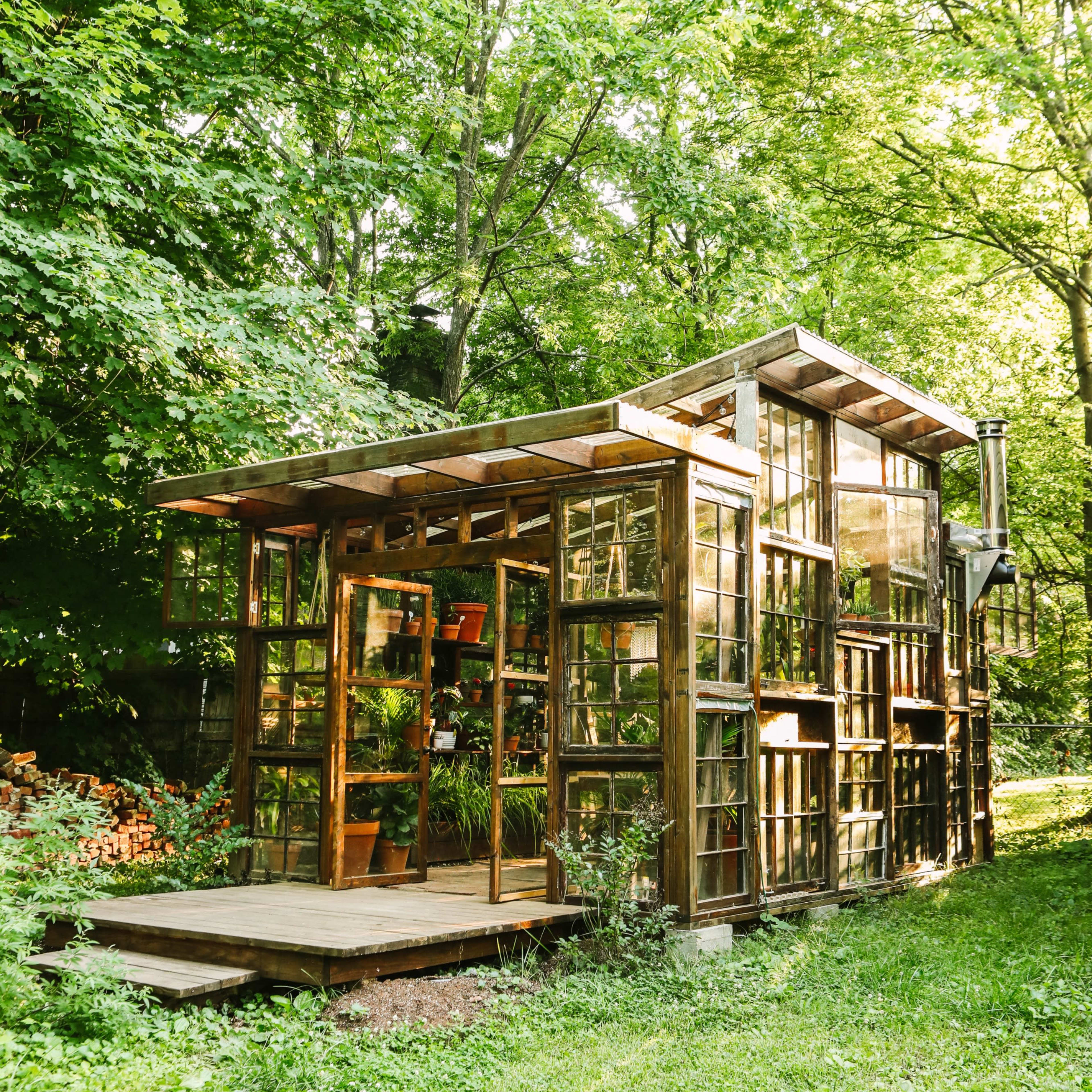 A wooden structure with numerous glass panels sits in a grassy area surrounded by trees.