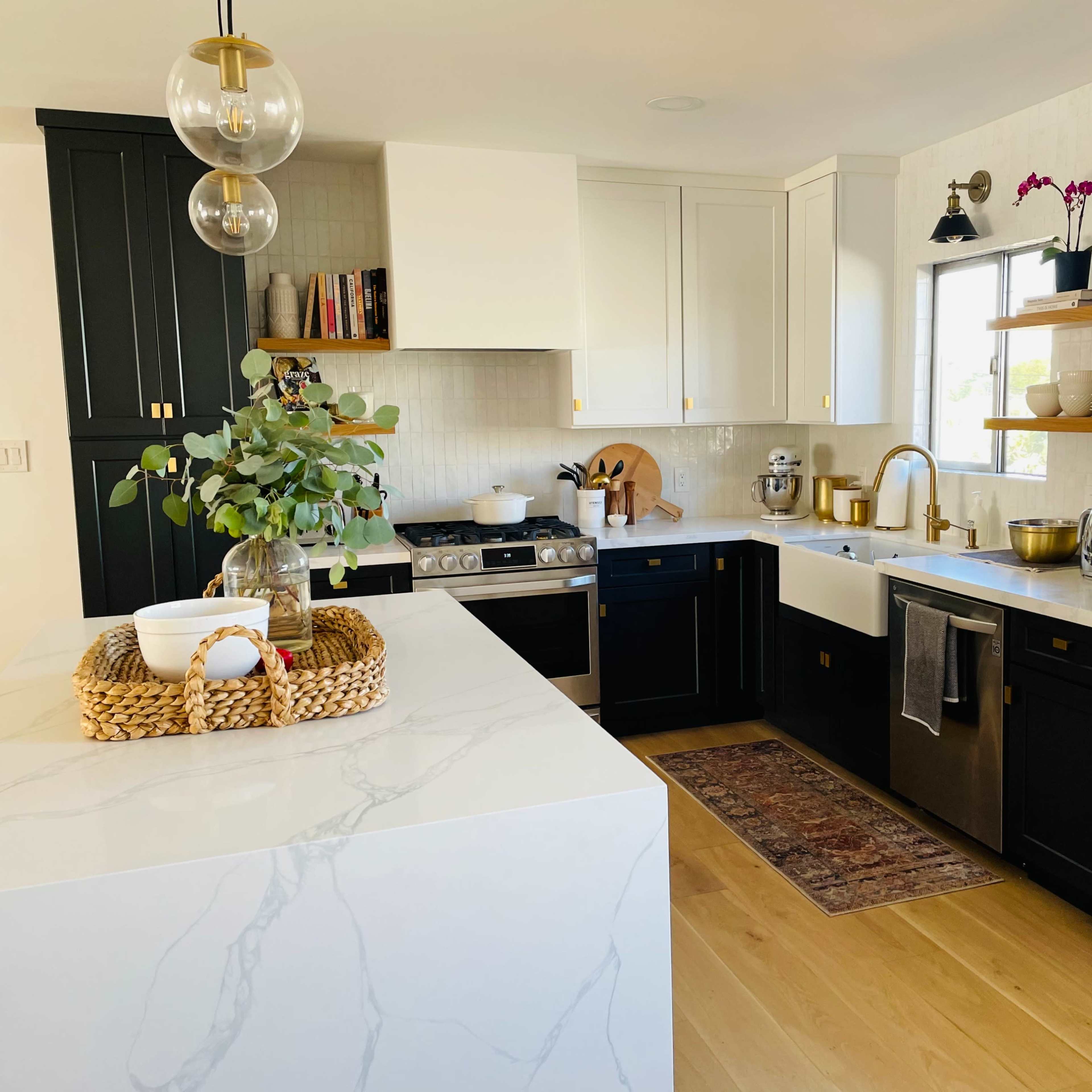 A modern kitchen with a marble island, black and white cabinetry, stainless steel appliances, and wooden shelves displaying kitchenware.