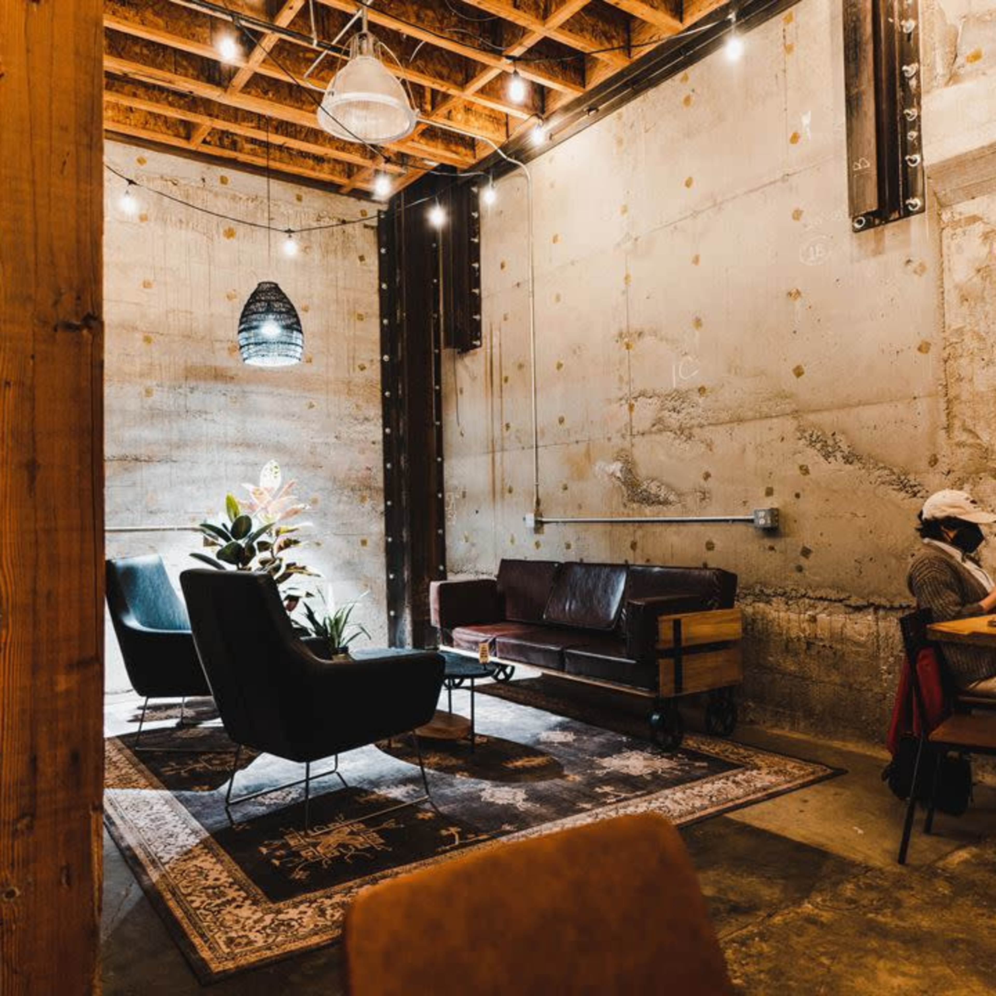 A cozy interior of a café with industrial design elements, featuring a mix of seating options, potted plants, and warm lighting.
