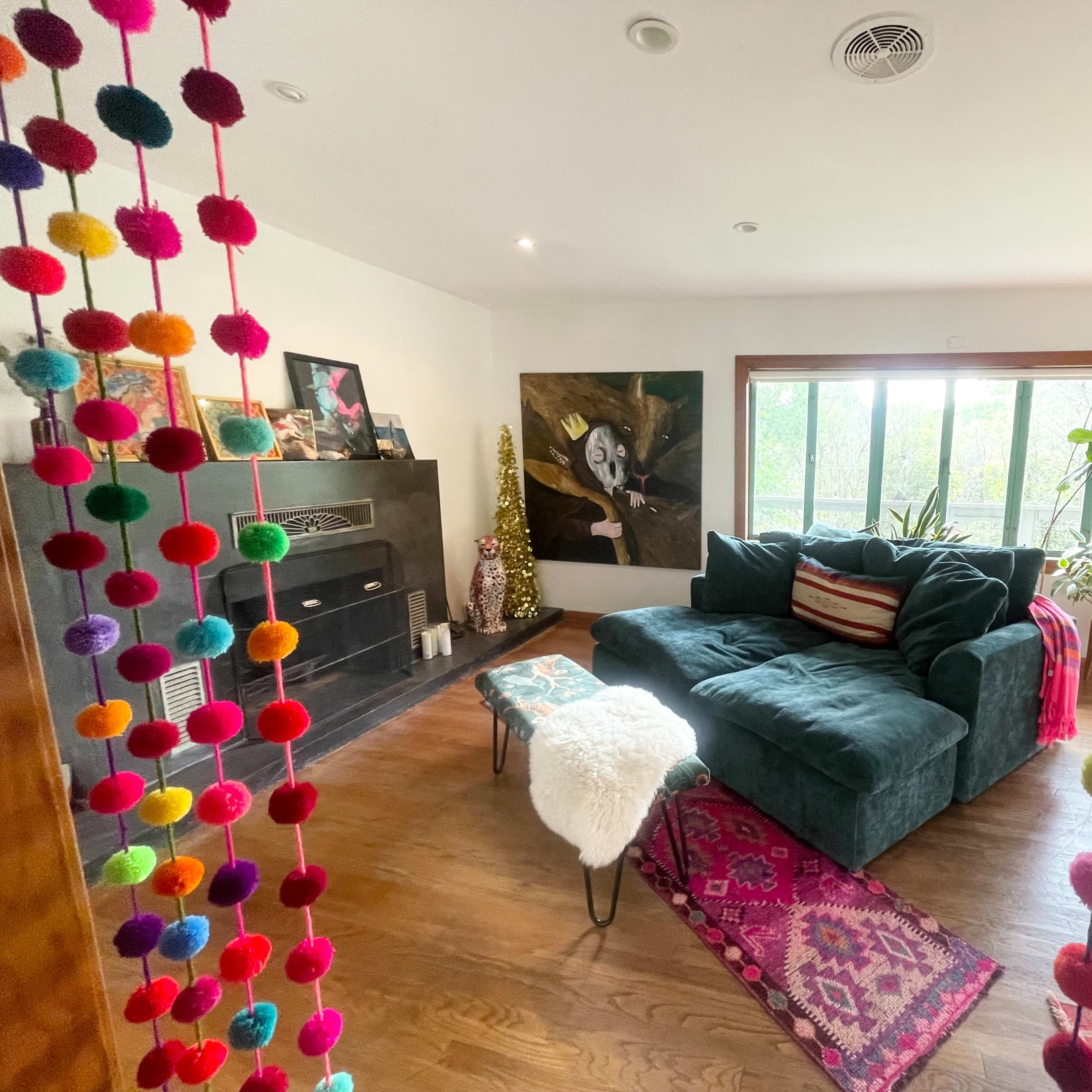 A cozy living room with a green couch, a patterned rug, and colorful pom-pom decorations hanging in the foreground.