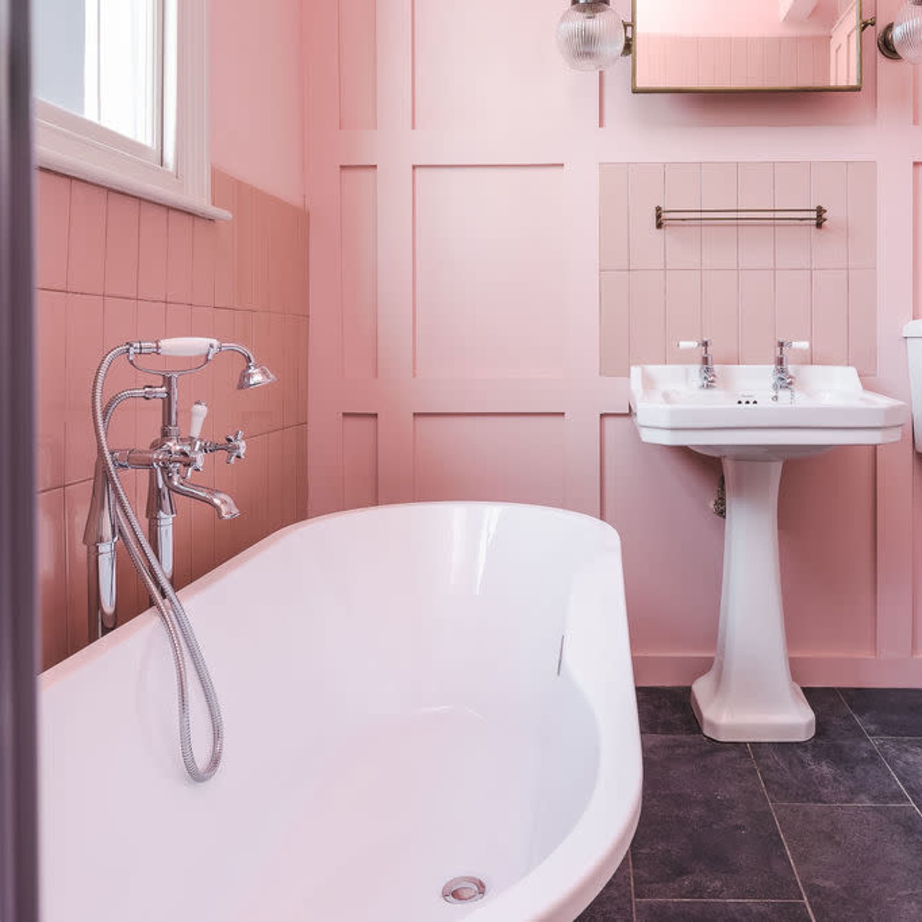 The bathroom features a freestanding bathtub, a sink with two faucets, a toilet, and pink paneled walls.