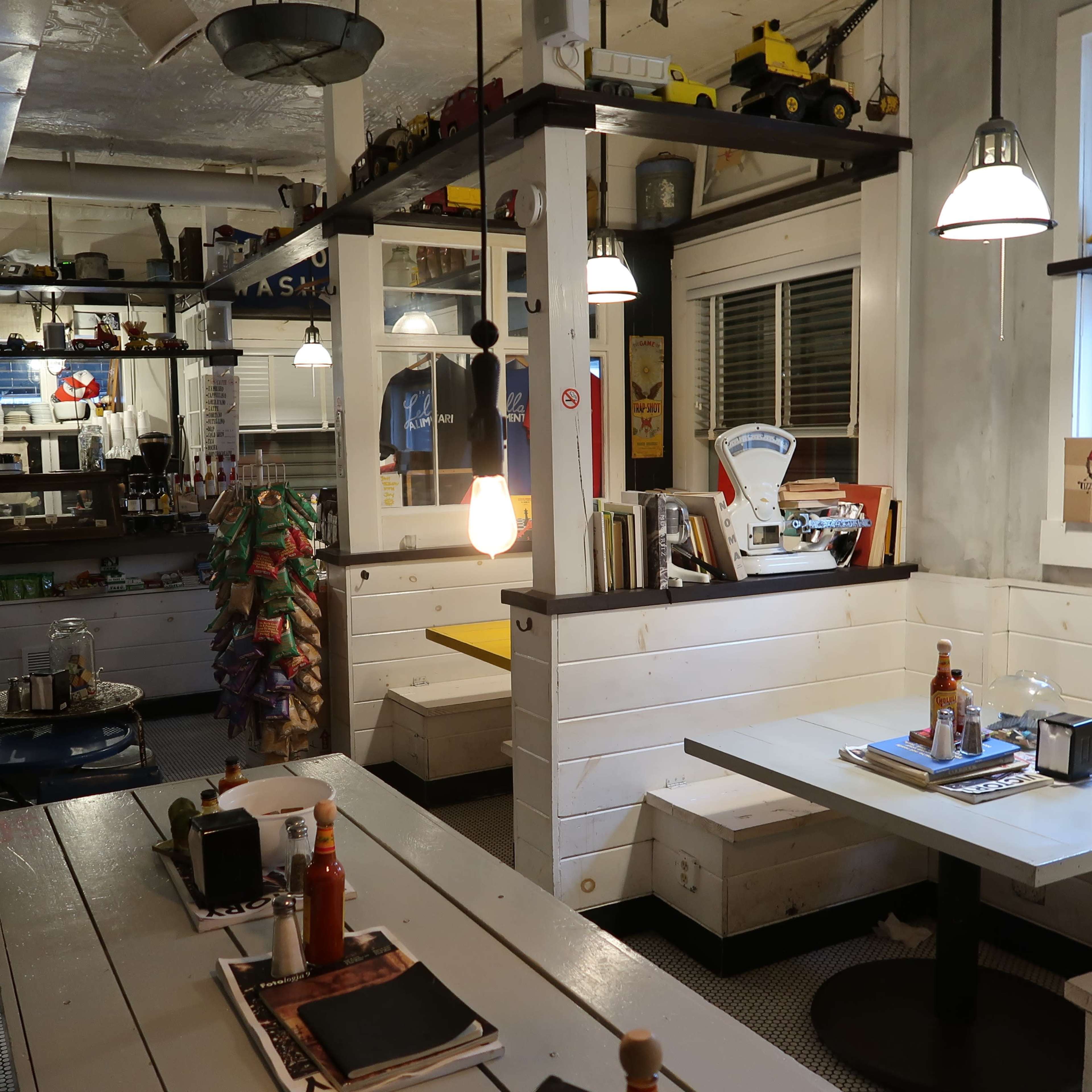 A modern diner interior with wooden tables, white benches, and decorative items on shelves and walls.