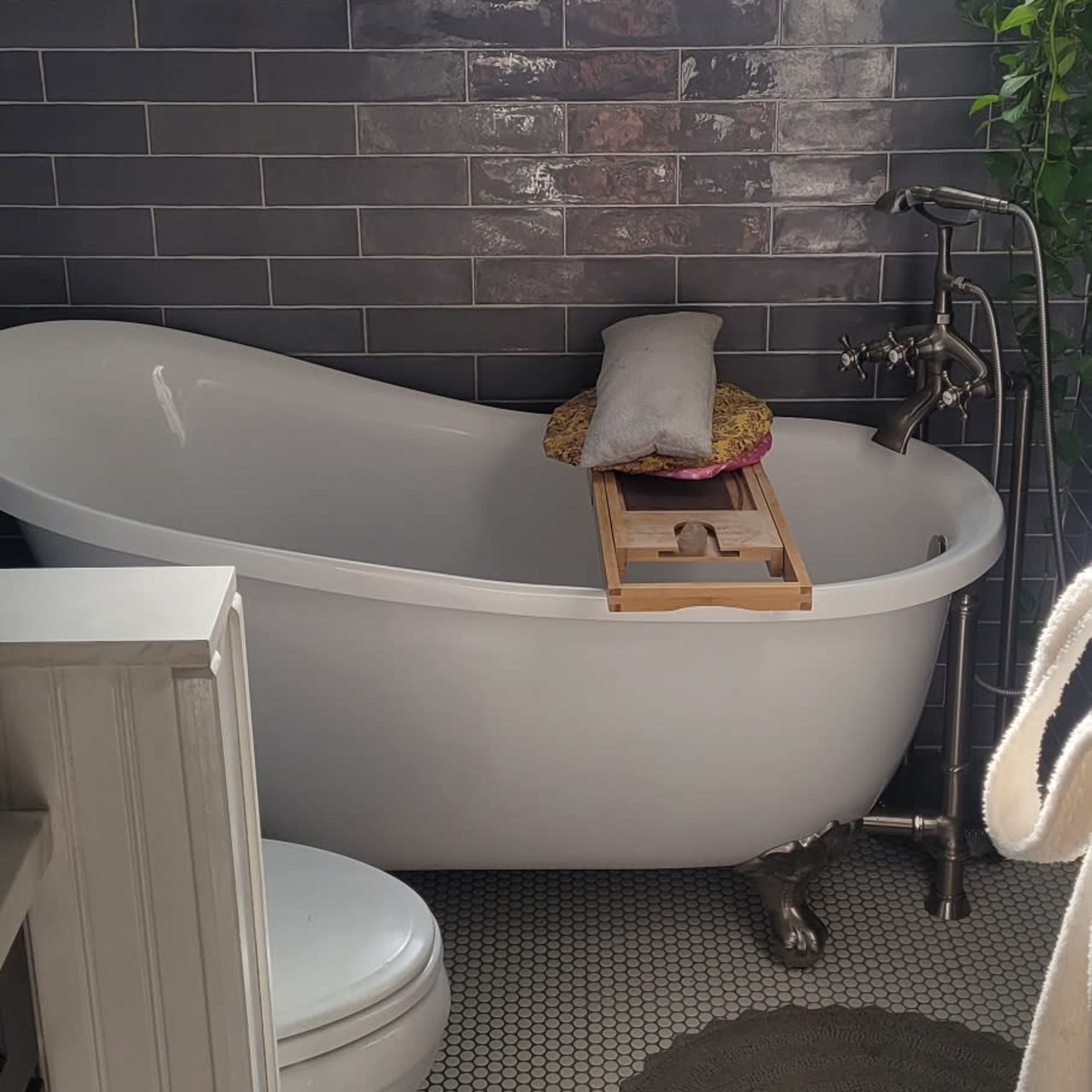 A bathroom featuring a freestanding bathtub, a toilet, a tiled wall, and a small rug on a patterned floor.