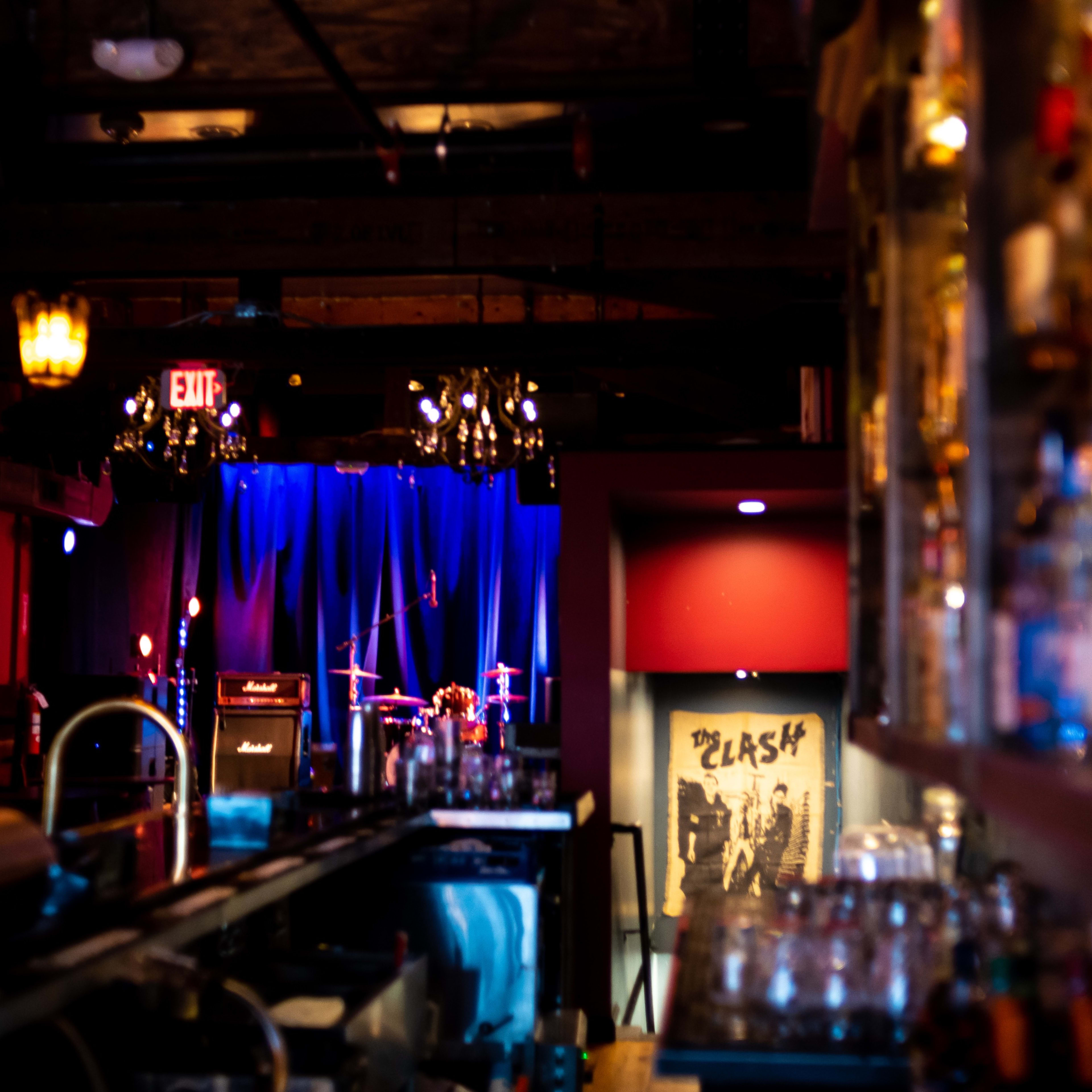The interior of a bar features a dimly lit stage with musical instruments and a bar counter lined with glassware.