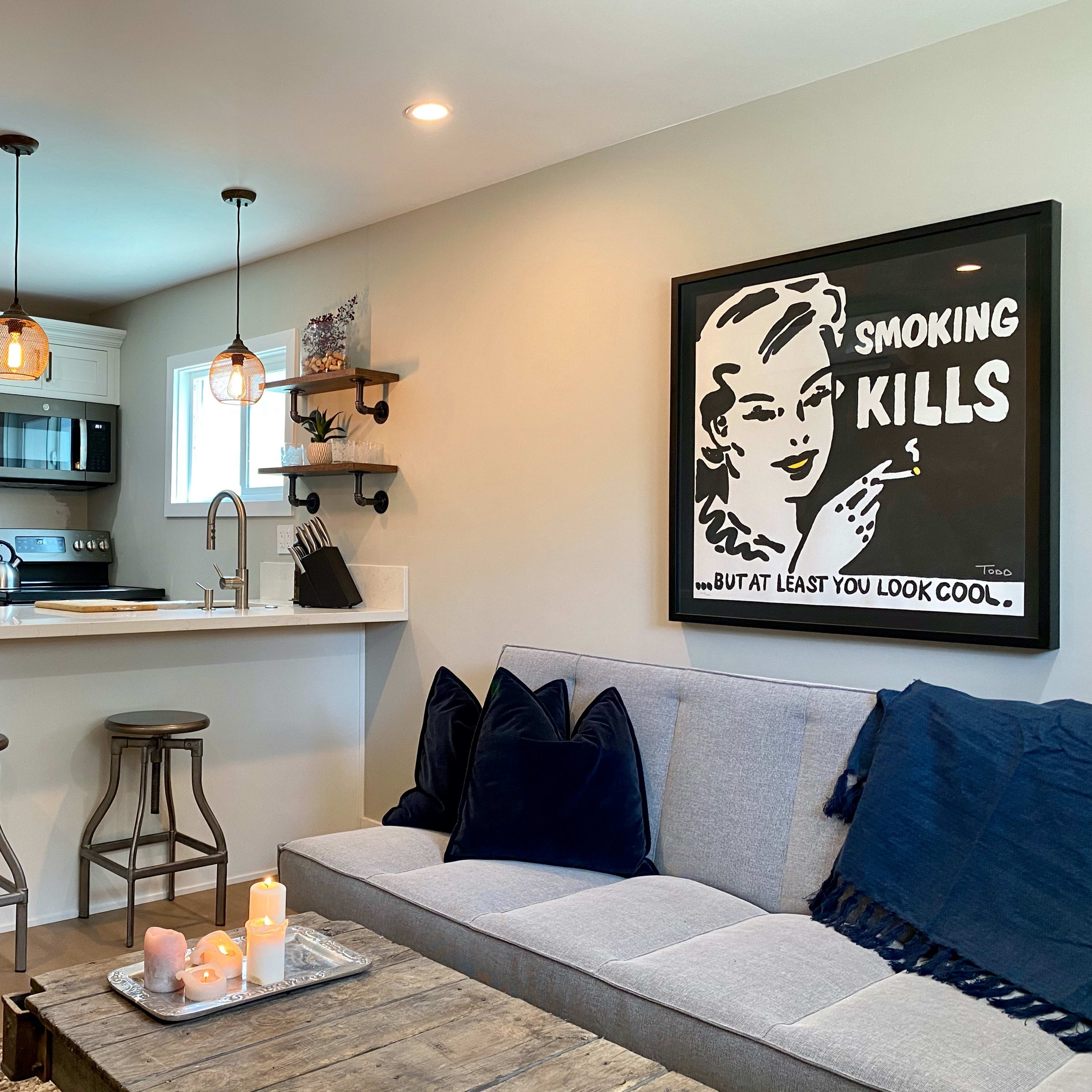 A modern kitchen and living area with a gray sofa, a wooden coffee table, and a kitchen island with bar stools.