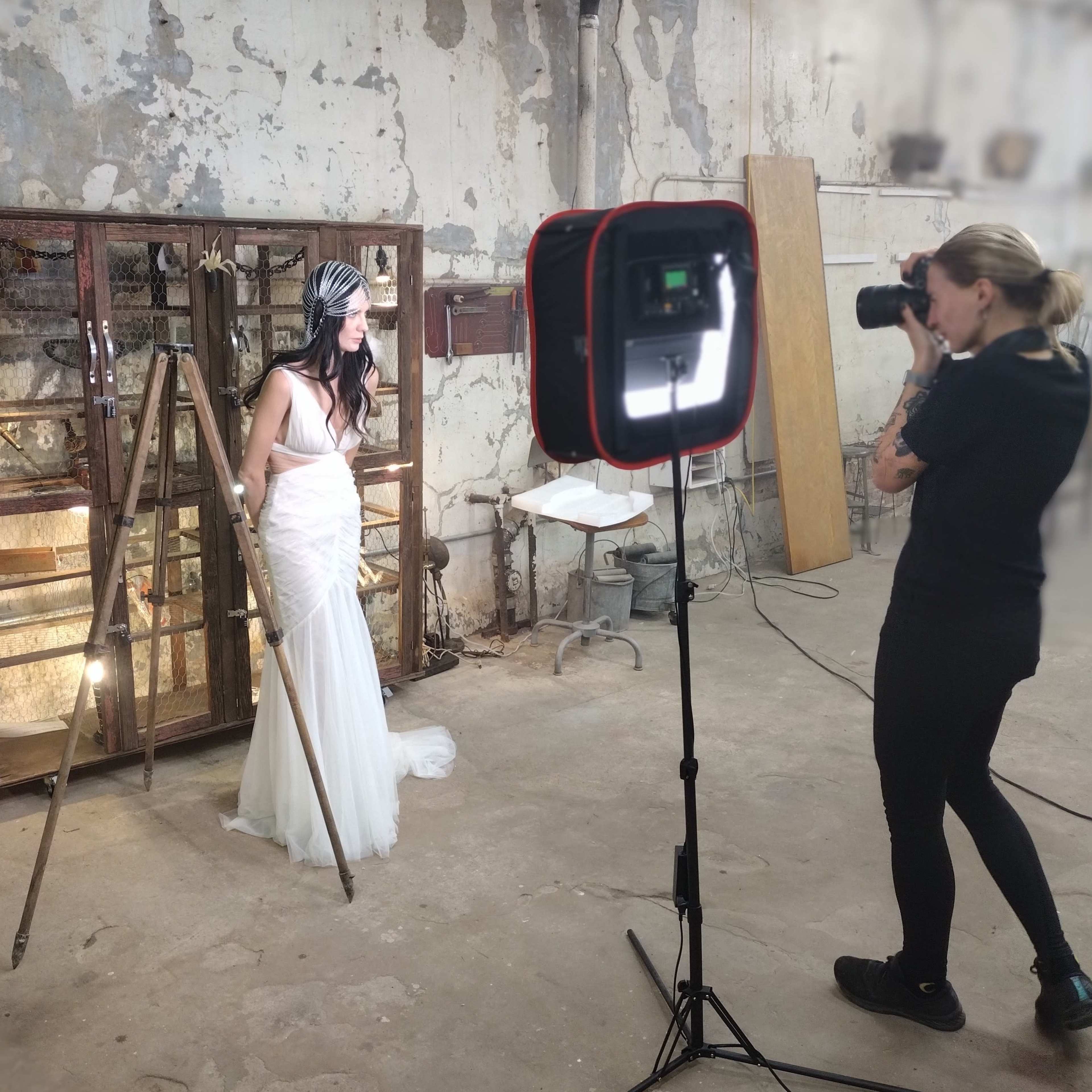 A bride in a white dress poses with a stick in front of a glass display cabinet while a photographer captures the scene.