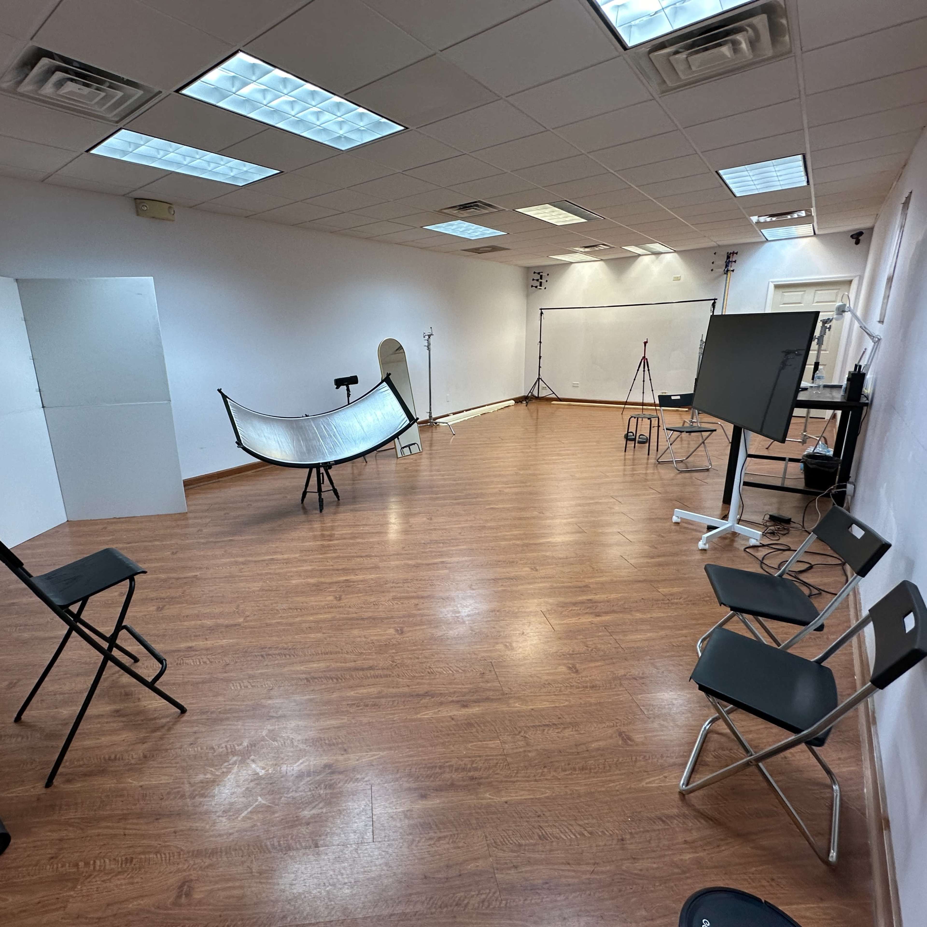 A spacious, empty studio with wooden flooring, several photography backdrops, and various equipment set up for shoots.