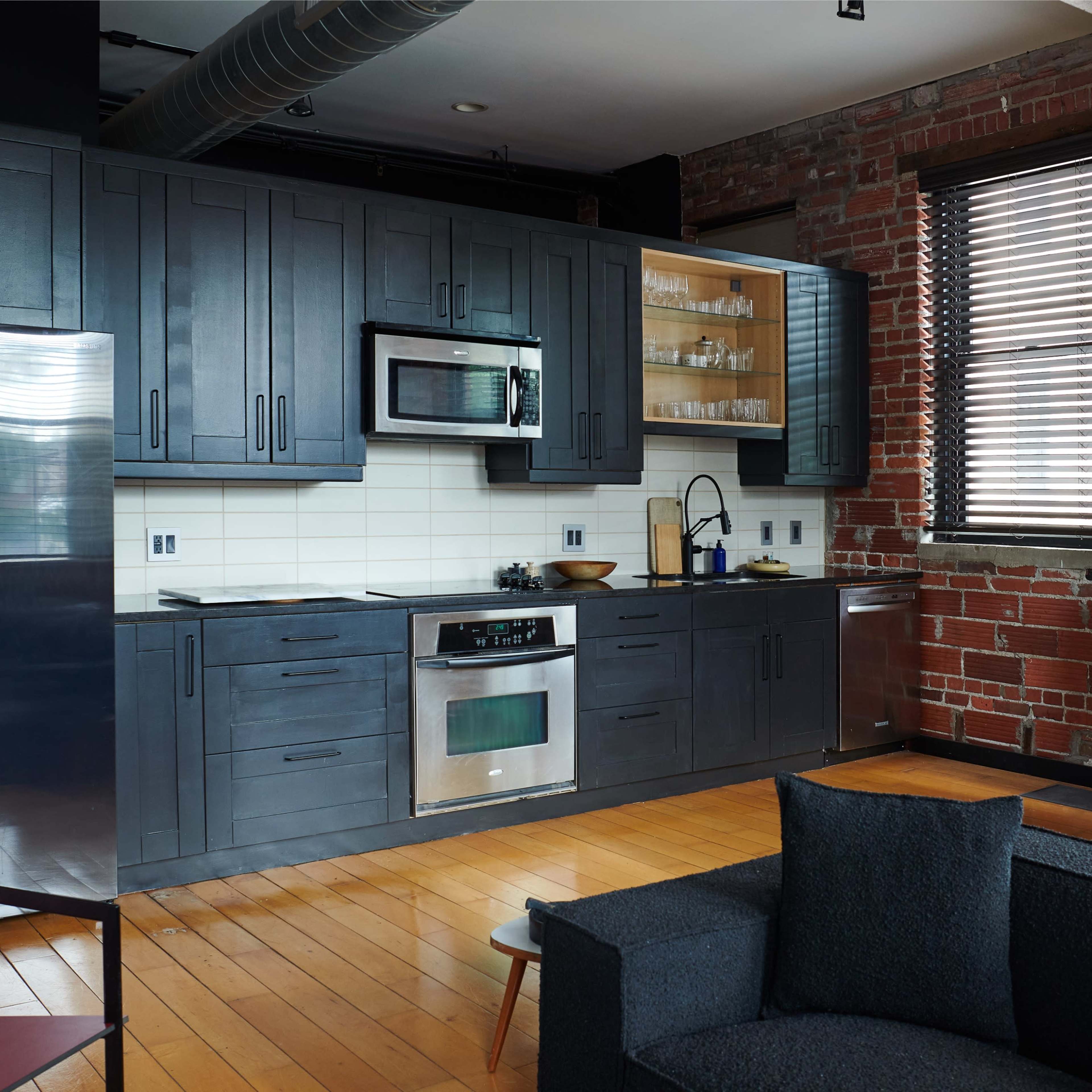 A modern kitchen featuring dark cabinetry, stainless steel appliances, and exposed brick walls.