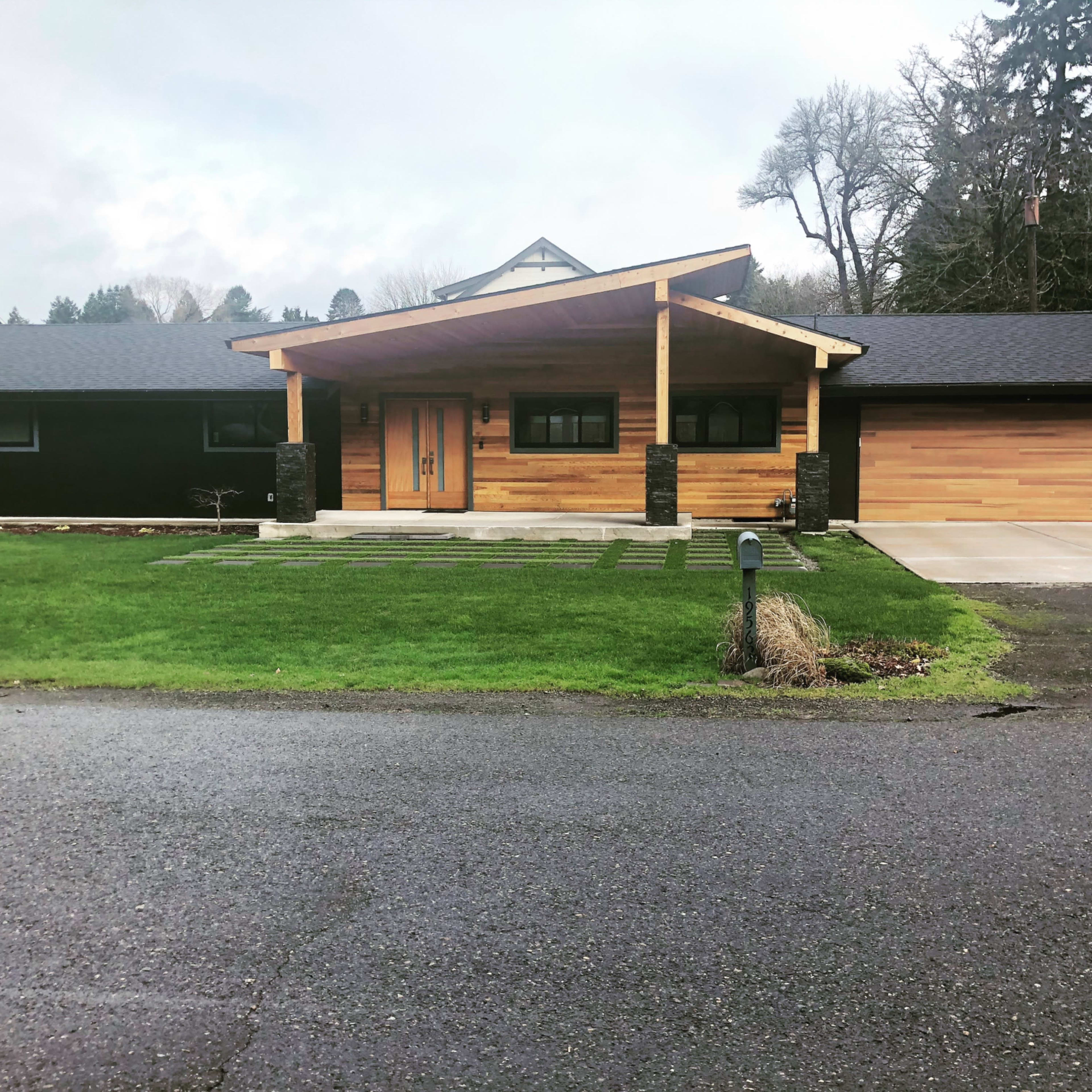 A modern single-story house with a wooden facade, a large front porch, and a neatly landscaped lawn.