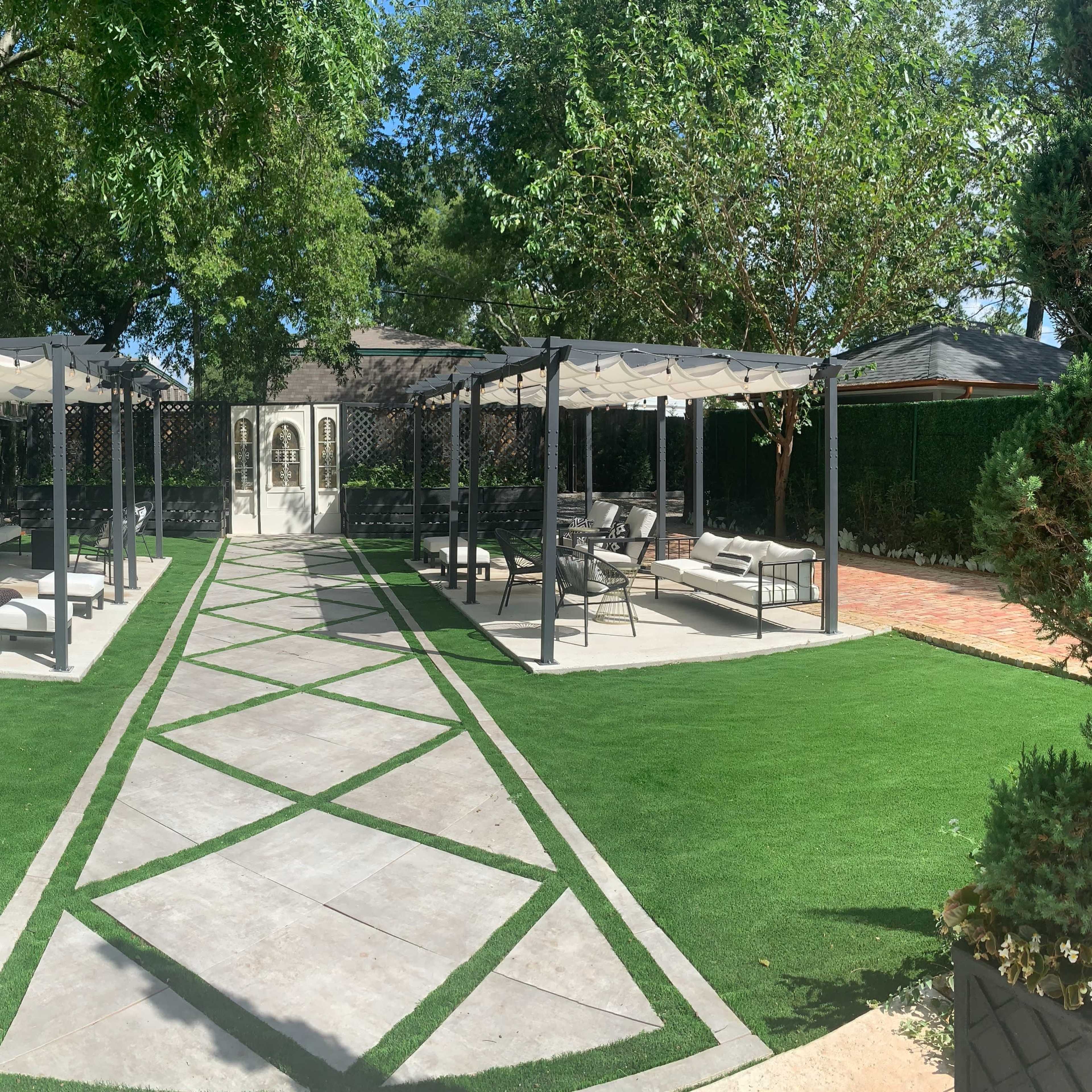A landscaped backyard featuring a central stone pathway bordered by artificial grass and two pergolas on either side, with seating areas under the structures.