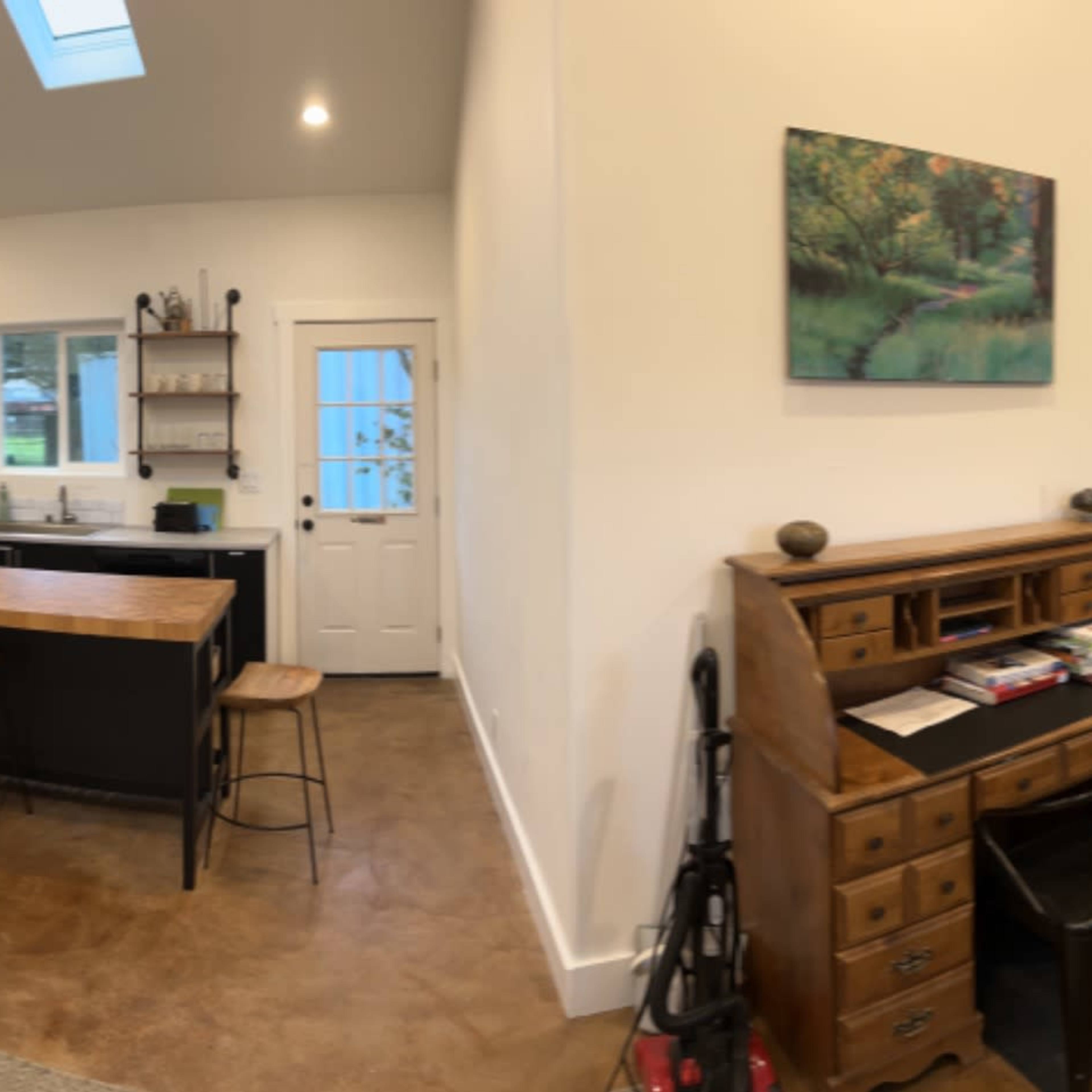 A bright, open-concept living space featuring a kitchen, dining area, and cozy seating arrangement with a mix of furniture, including a wooden table and a vintage-style dresser.