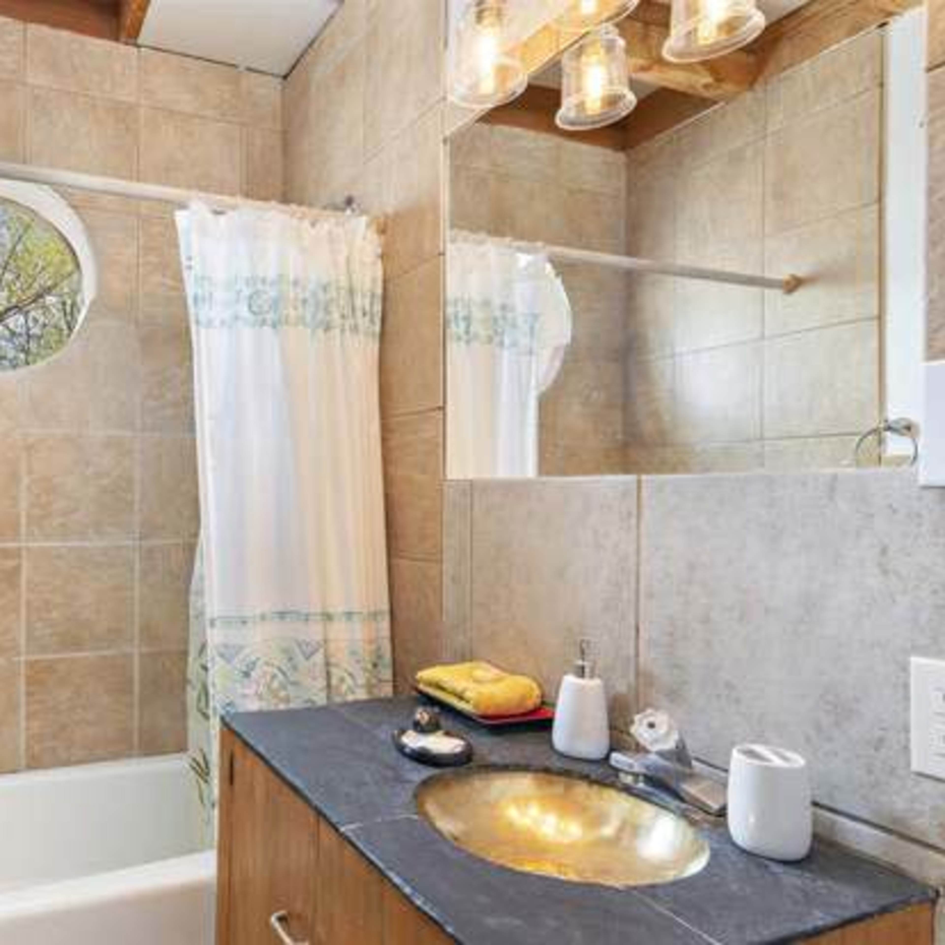 A bathroom with a bathtub, a circular window, a towel rack, and a mirrored vanity with toiletries.