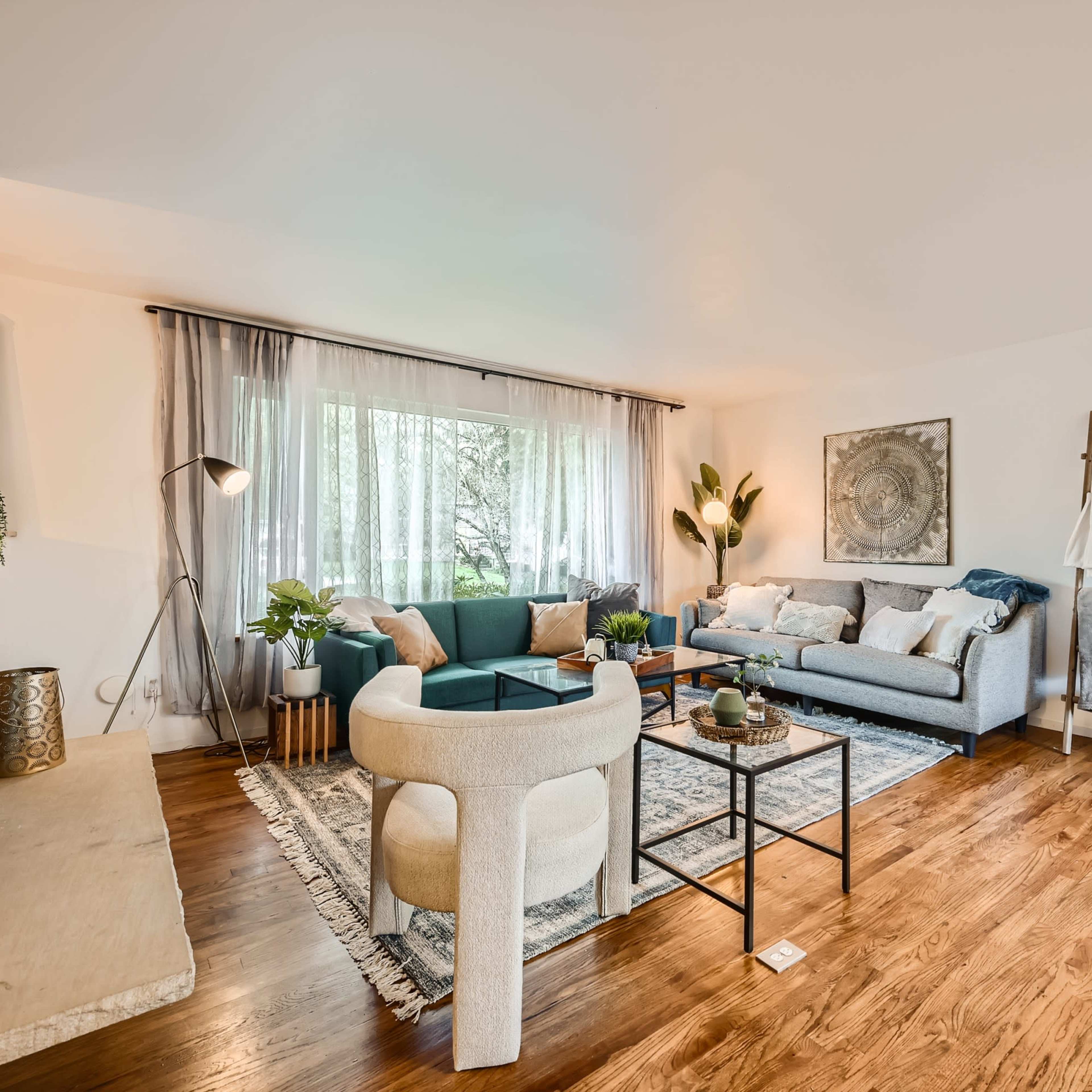 A modern living room with a sectional sofa, a round coffee table, a light-colored rug, a fireplace, and large windows allowing natural light to enter.