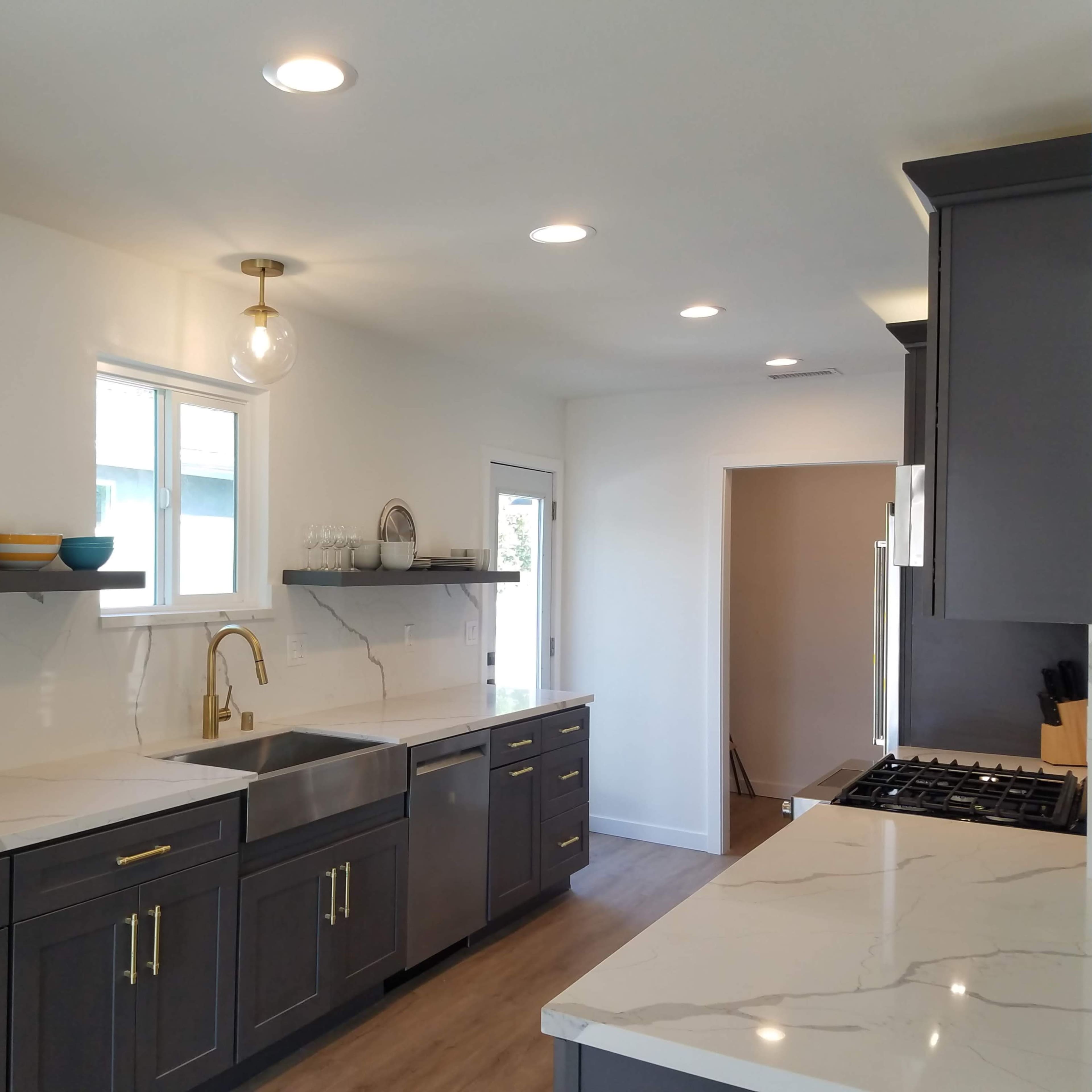 A modern kitchen features grey cabinetry, white marble countertops, and open shelving with decorative items.