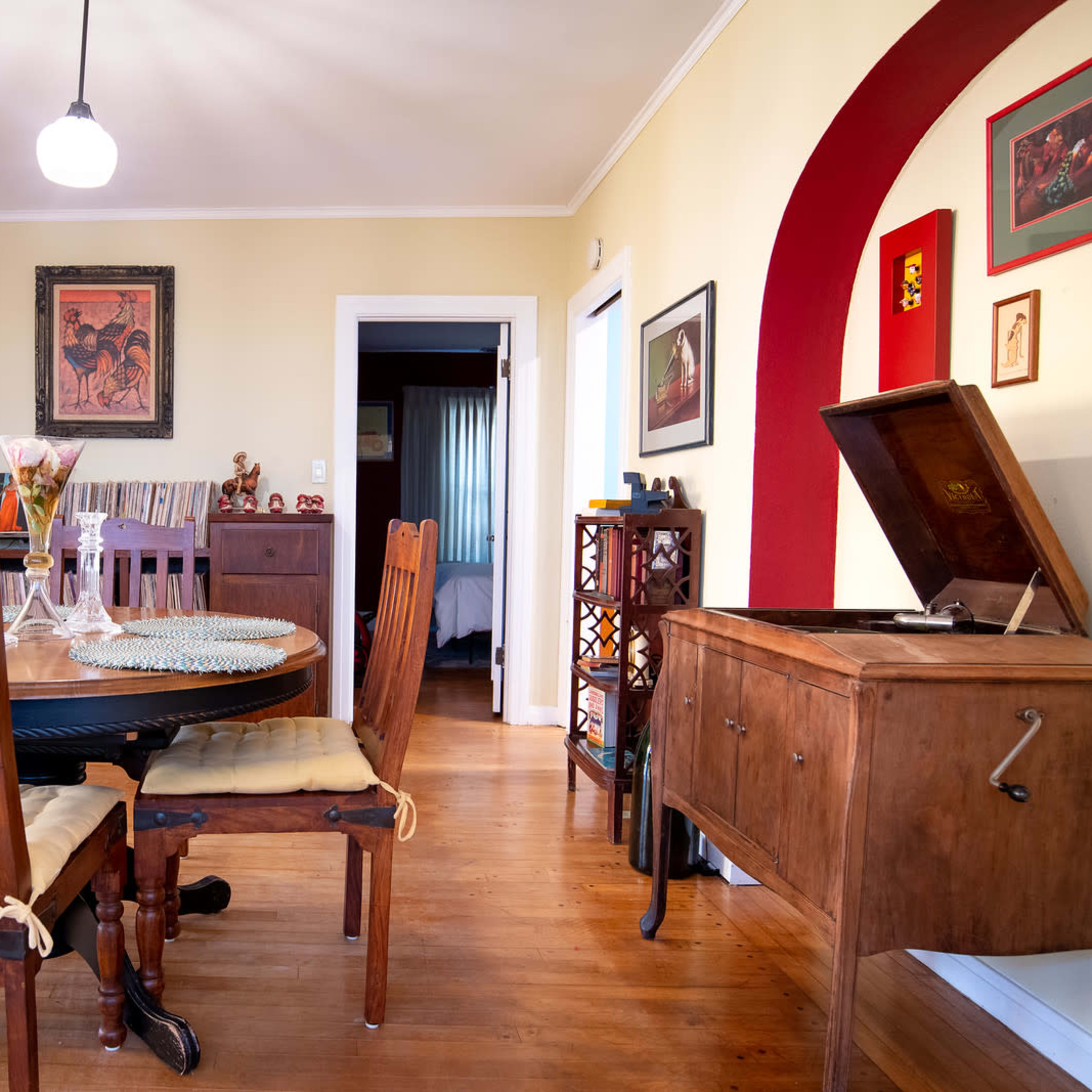 A cozy dining area featuring a wooden table surrounded by chairs, a record player, and various framed artworks on the walls.